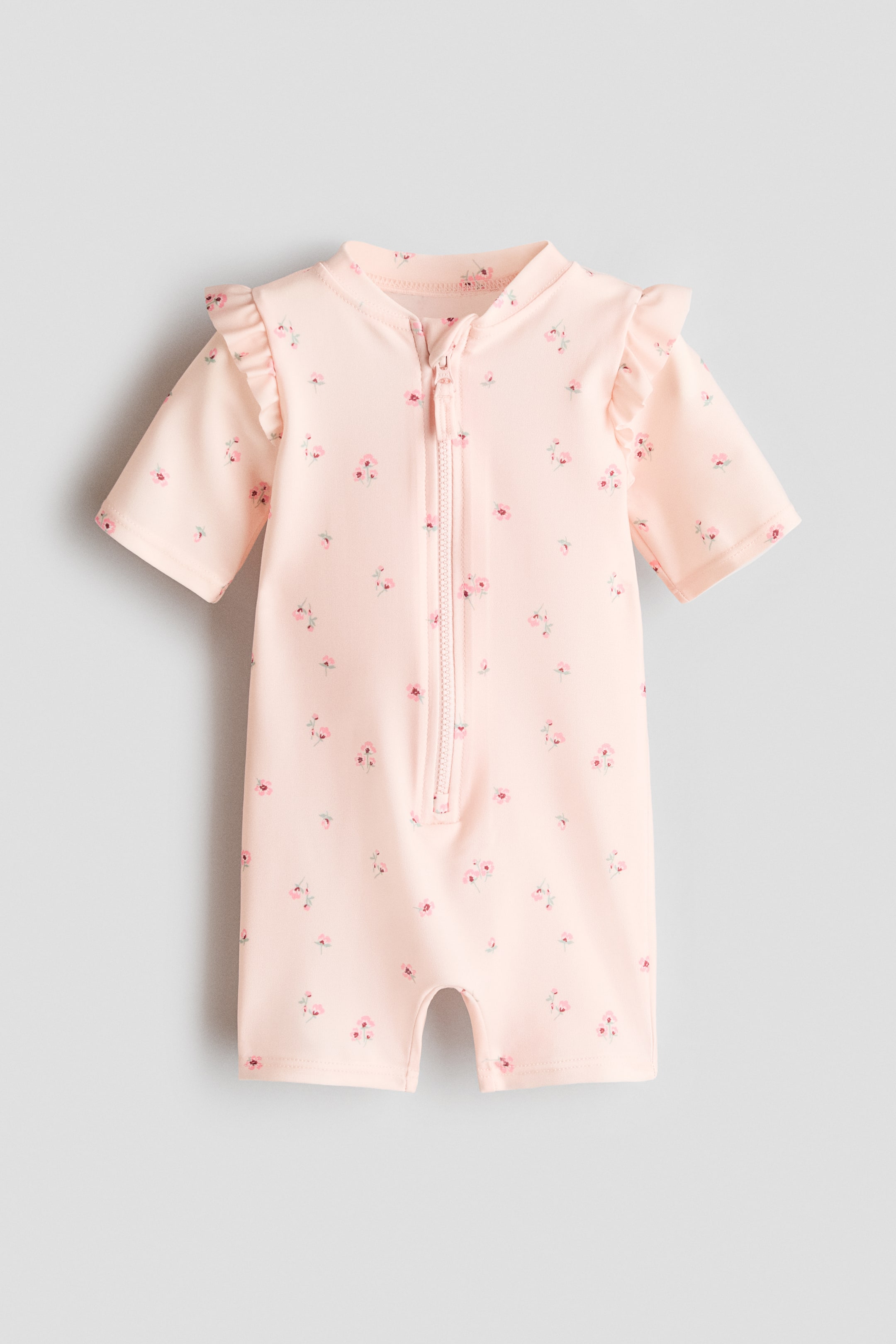 Visualizza immagine più grande: Costume da bagno rosa chiaro con una piccola stampa floreale in tonalità di rosa, caratterizzato da un colletto alto, una zip frontale, maniche corte con spalle arricciate e gambe corte, presentando la sua parte anteriore.
