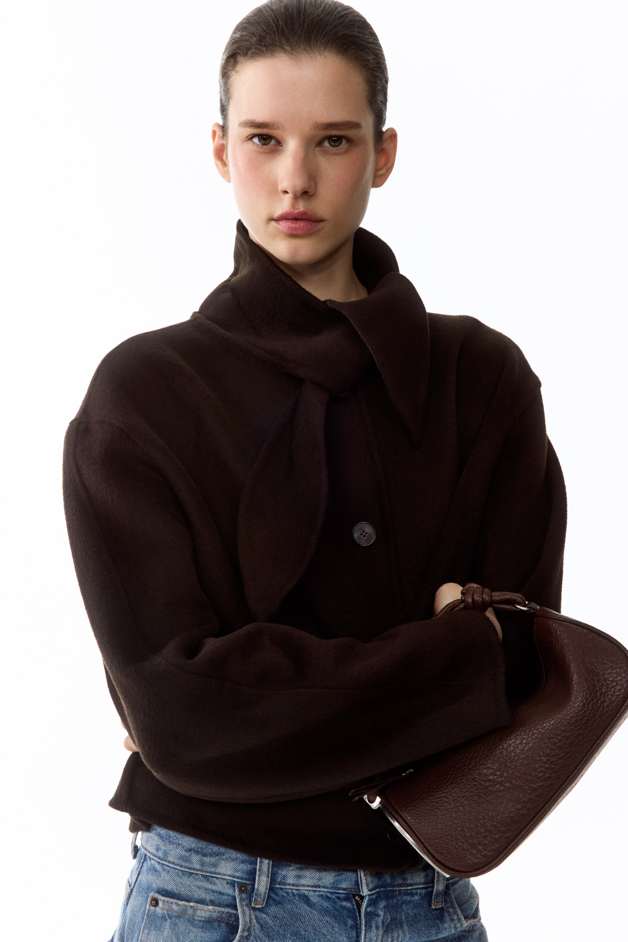 Agrandir l'image: Une veste marron foncé présente un col haut drapé avec de larges panneaux avant croisés et une fermeture à bouton visible unique, mettant en valeur une coupe ample et des manches longues.