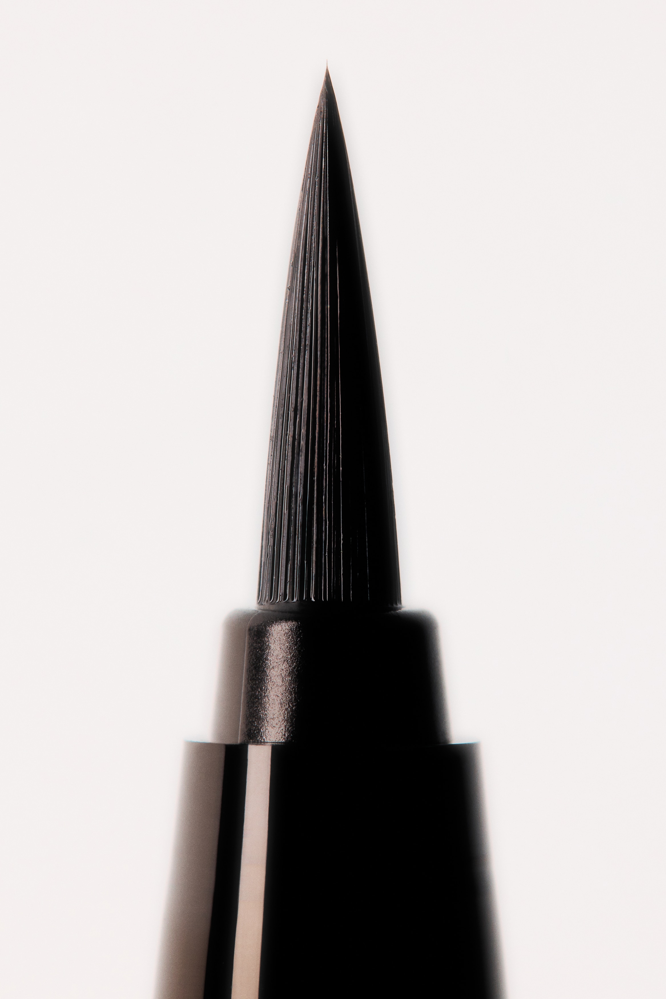 Een zilveren, reflecterende vloeibare eyeliner pen toont zijn twee delen rechtopstaand, één met dop en de ander zonder dop om een zwarte viltstiftapplicator te onthullen. Beide delen hebben "MASTERSTROKE EYELINER" in rode tekst langs de voorkant.