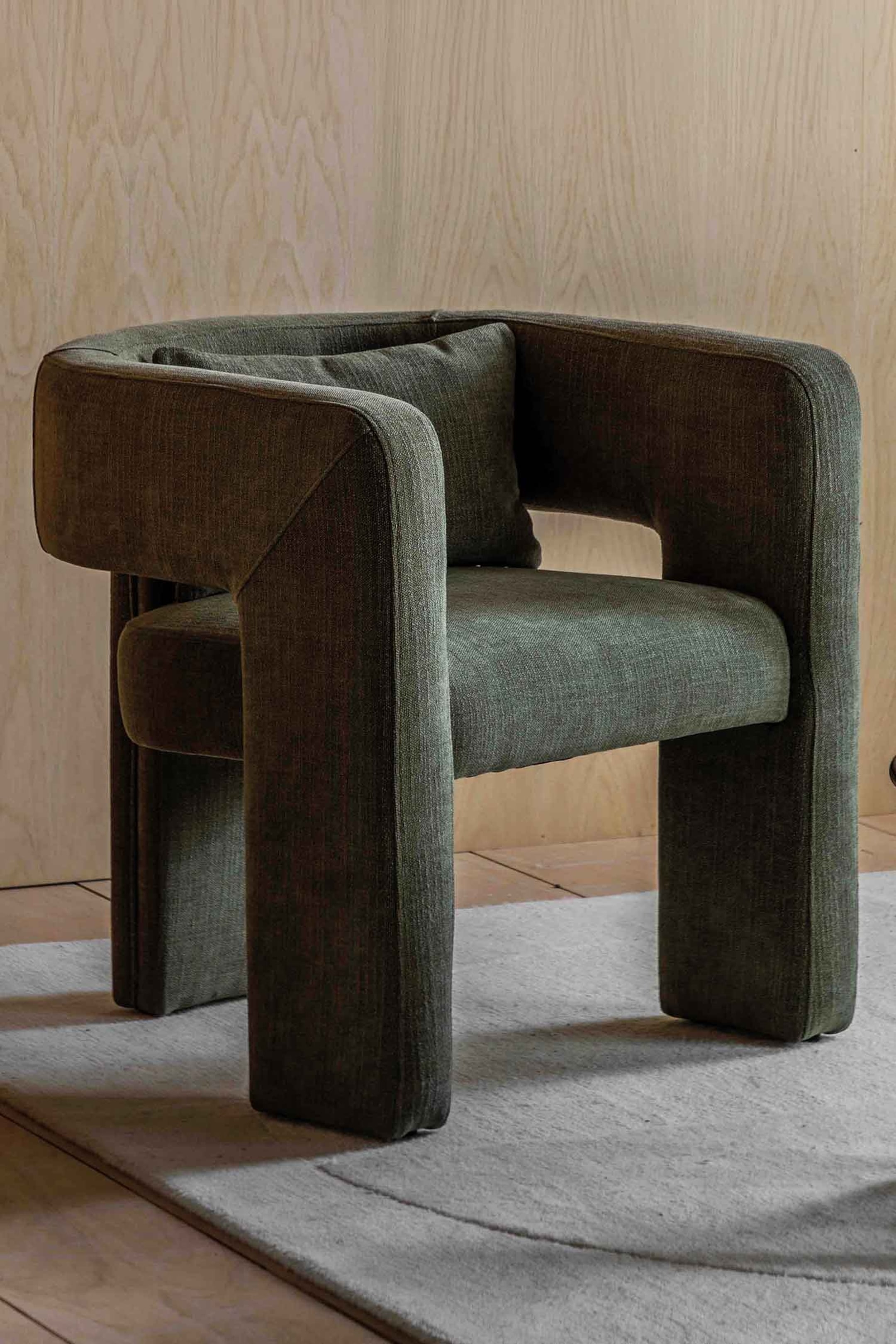 View larger image: A dark green upholstered chair, crafted from textured woven fabric, is positioned at a slight angle to the right, showcasing its wide, rectilinear armrests and integrated legs. A small, matching rectangular cushion rests against its backrest, with a visible gap between the seat and the backrest.