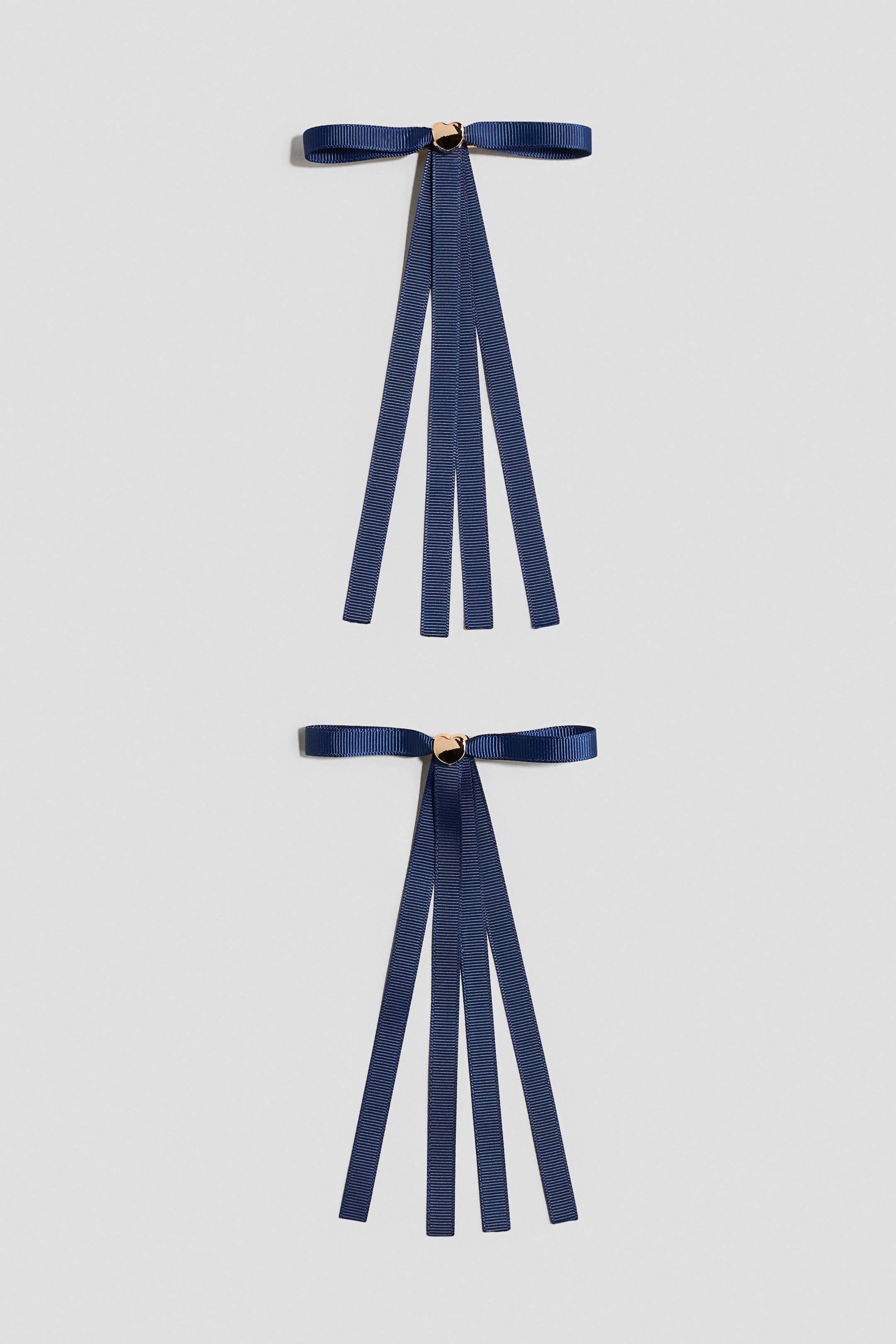 View larger image: Two identical navy blue ribbon bows are displayed, each forming a classic bow with two horizontal loops and tails. Three narrower navy blue ribbon strips are extending vertically from the centre of each bow, where a small gold-toned heart accent is securing them.