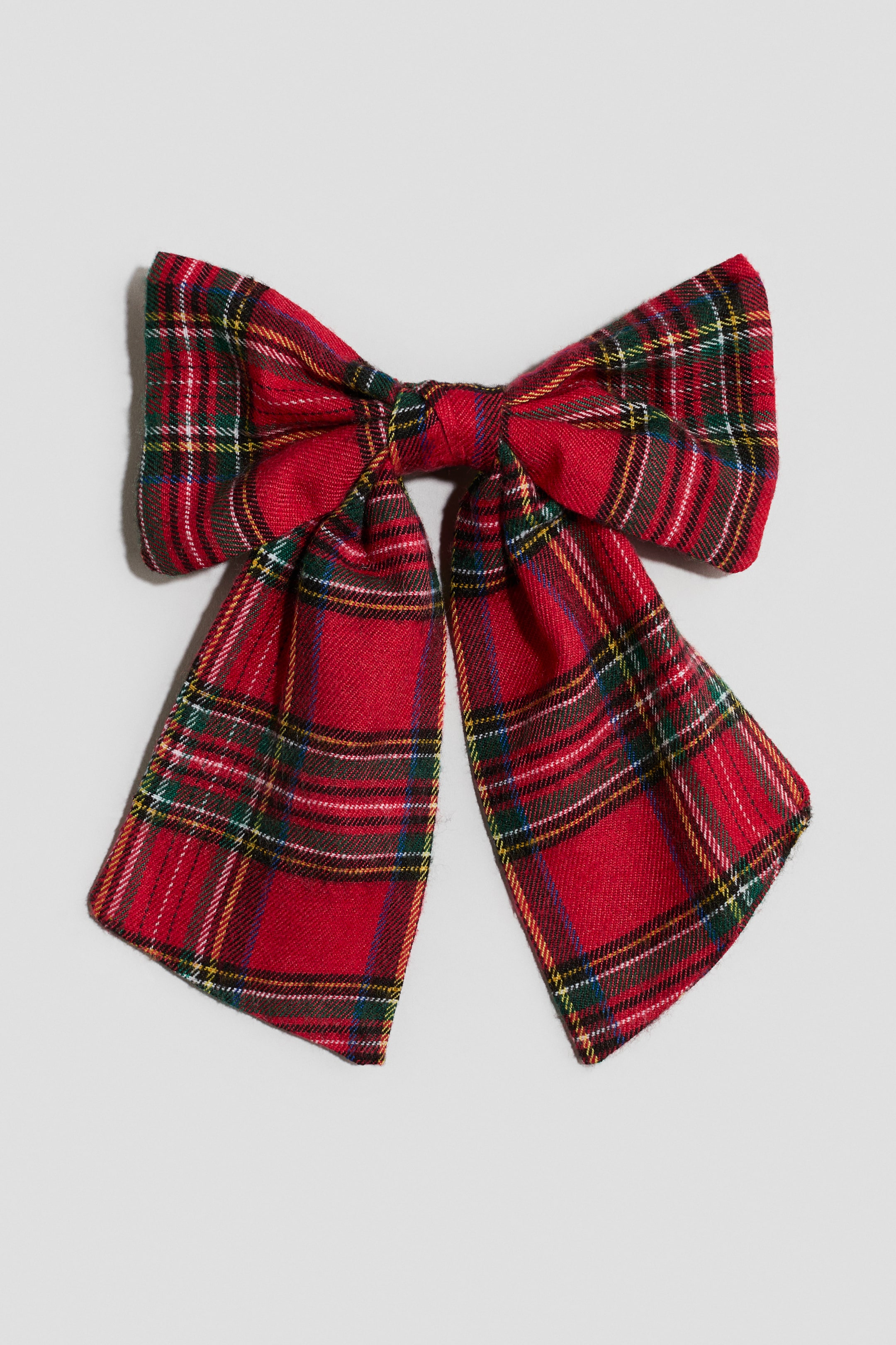 Visualizza l'immagine ingrandita: Una molletta per capelli con un grande fiocco in morbido tessuto tartan rosso è mostrata frontalmente, mettendo in risalto due ampie estremità che scendono verso il basso. Il tessuto presenta un classico motivo a quadri con strisce intrecciate verdi, gialle, nere e bianche.