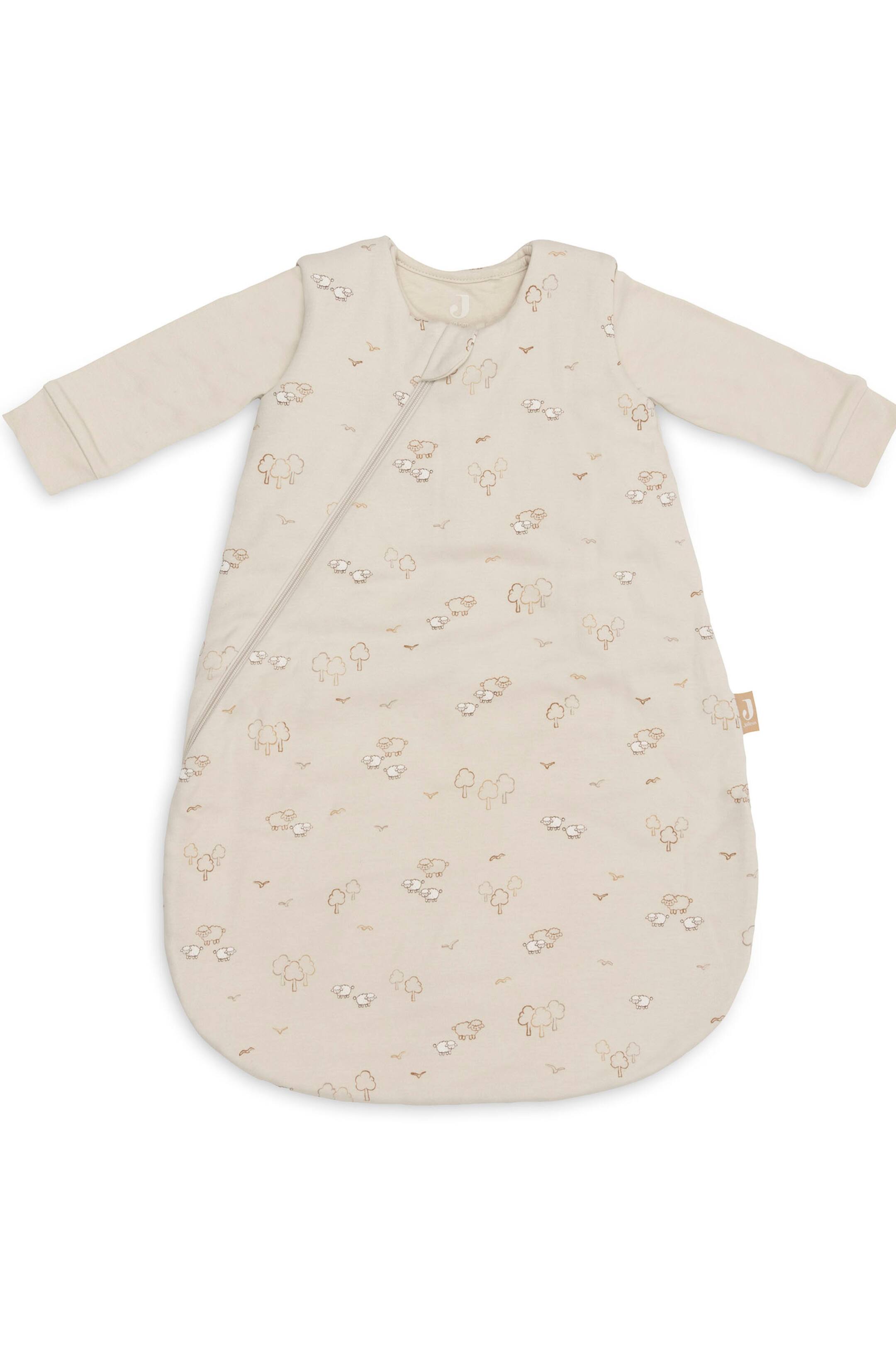 Größeres Bild anzeigen: Ein hellbeiger Babyschlafsack ist in einer Flat-Lay-Ansicht von vorne zu sehen, mit langen Ärmeln mit Rippbündchen und einem abgerundeten Sackboden. Das Design zeigt ein durchgehendes Muster aus kleinen Schafen, Bäumen und Vögeln, mit einem diagonalen Reißverschluss, der vom Kragen entlang der linken Seite verläuft.