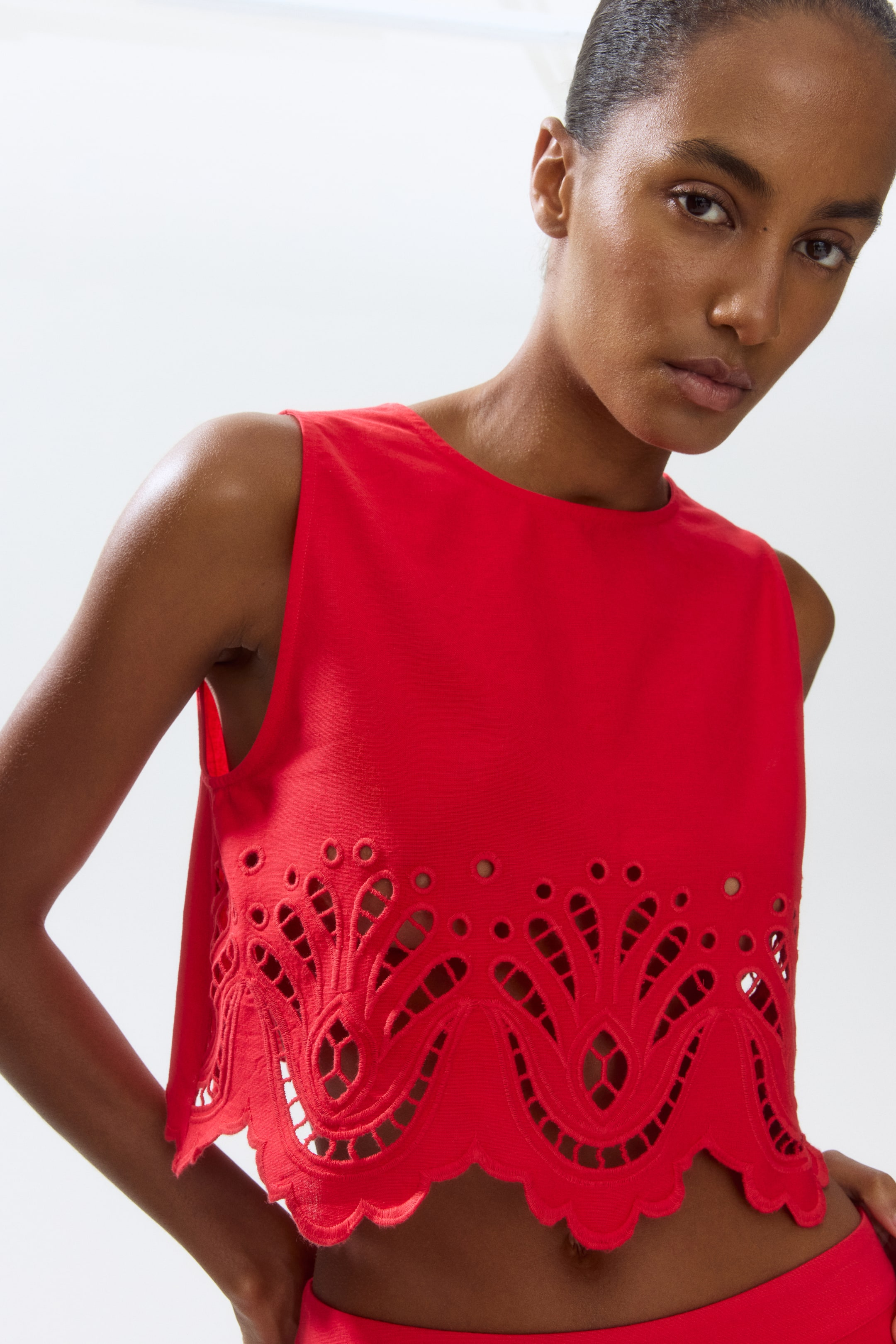 View larger image: "A red sleeveless top featuring a round neckline and a cropped length. It showcases intricate broderie anglaise detailing with a scalloped edge along its hem."