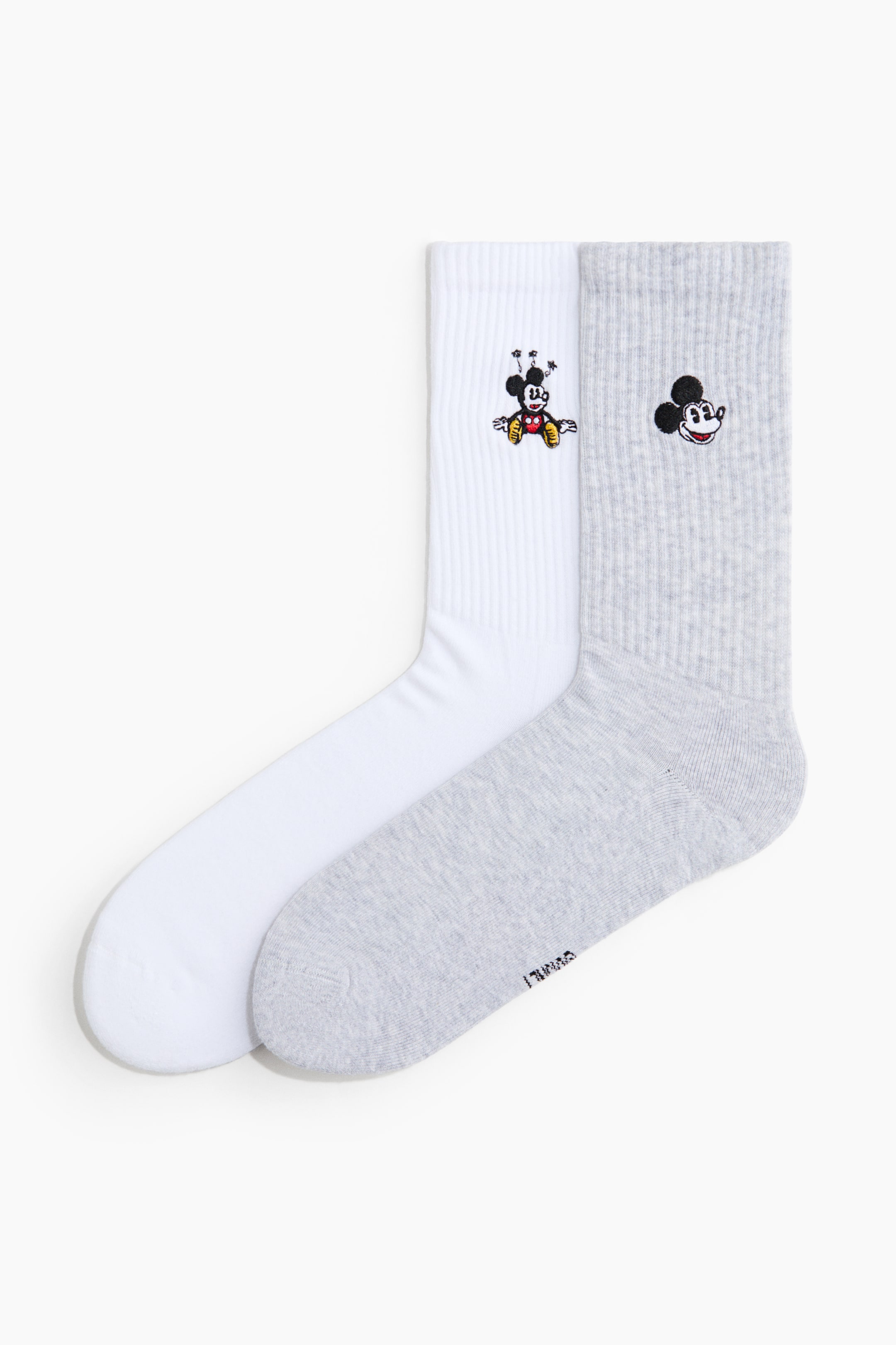 Büyük resmi görüntüle: İki çift çorap sunulmaktadır: beyaz bir çift ve açık gri bir çift, her ikisi de yüksek, nervürlü şaftlara sahiptir. Beyaz çorap, tam vücut Mickey Mouse karakter motifi sergilerken, gri çorap Mickey Mouse kafa motifi sergilemektedir.