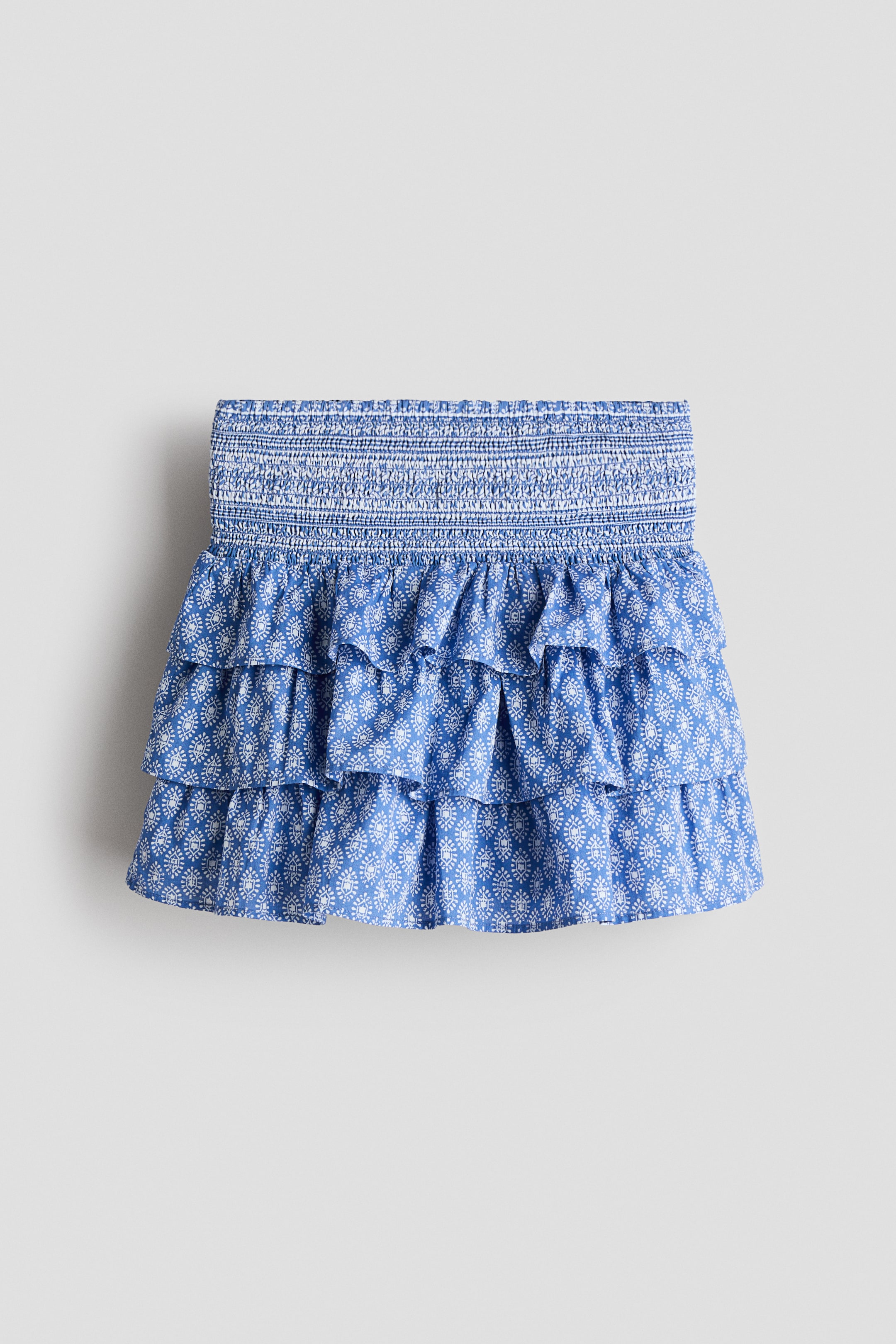 Προβολή μεγαλύτερης εικόνας: Μια μίνι φούστα με μπλε και λευκό μοτίβο διαθέτει σφηκοφωλιά στη μέση και τρία επίπεδα με βολάν.