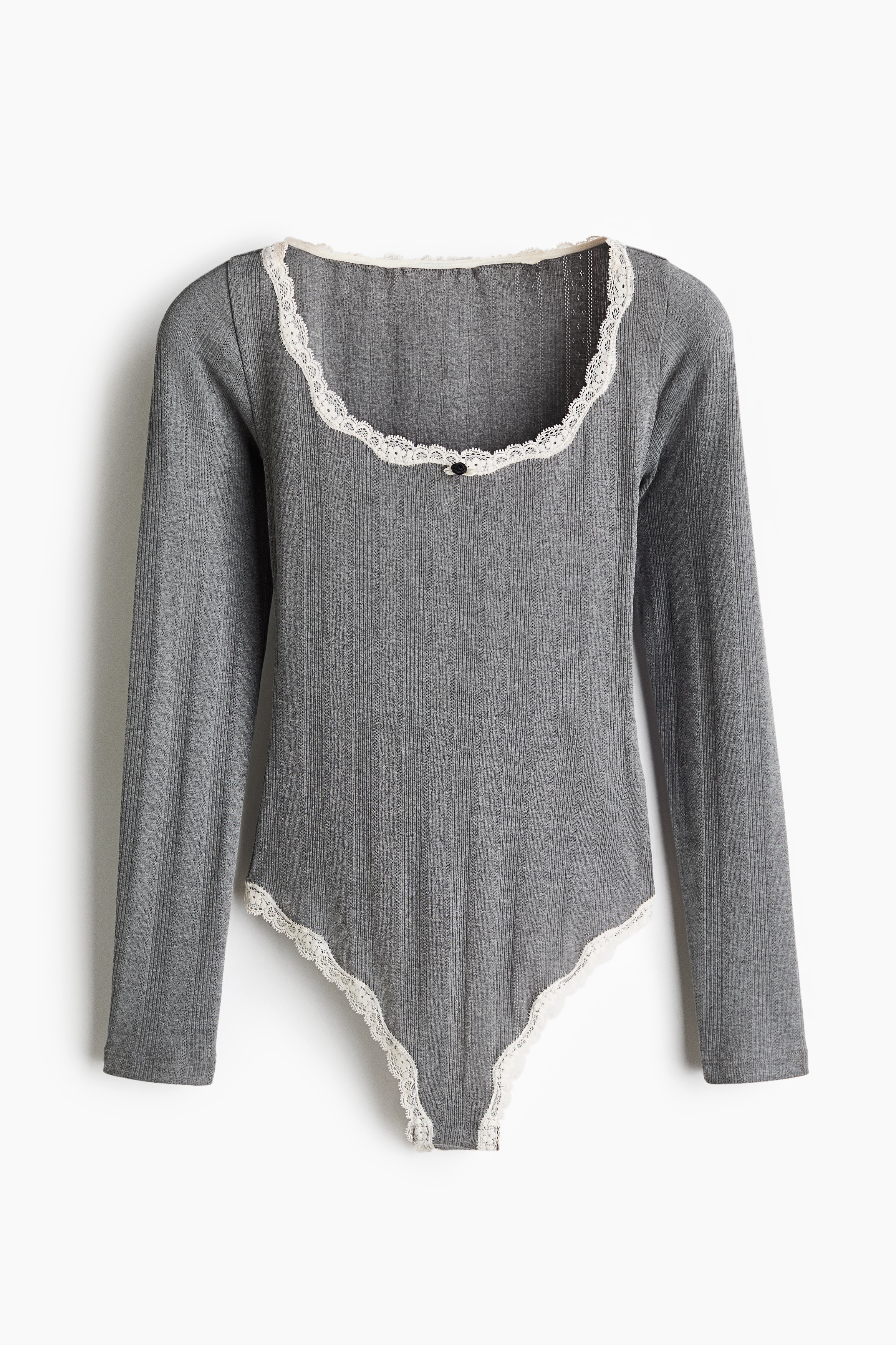 The grey, long-sleeved knitted bodysuit features white lace trim along the neckline and high-cut leg openings. It fits closely to the body in a side-profile view, styled with low-rise white trousers that reveal the lace detailing at the hip.