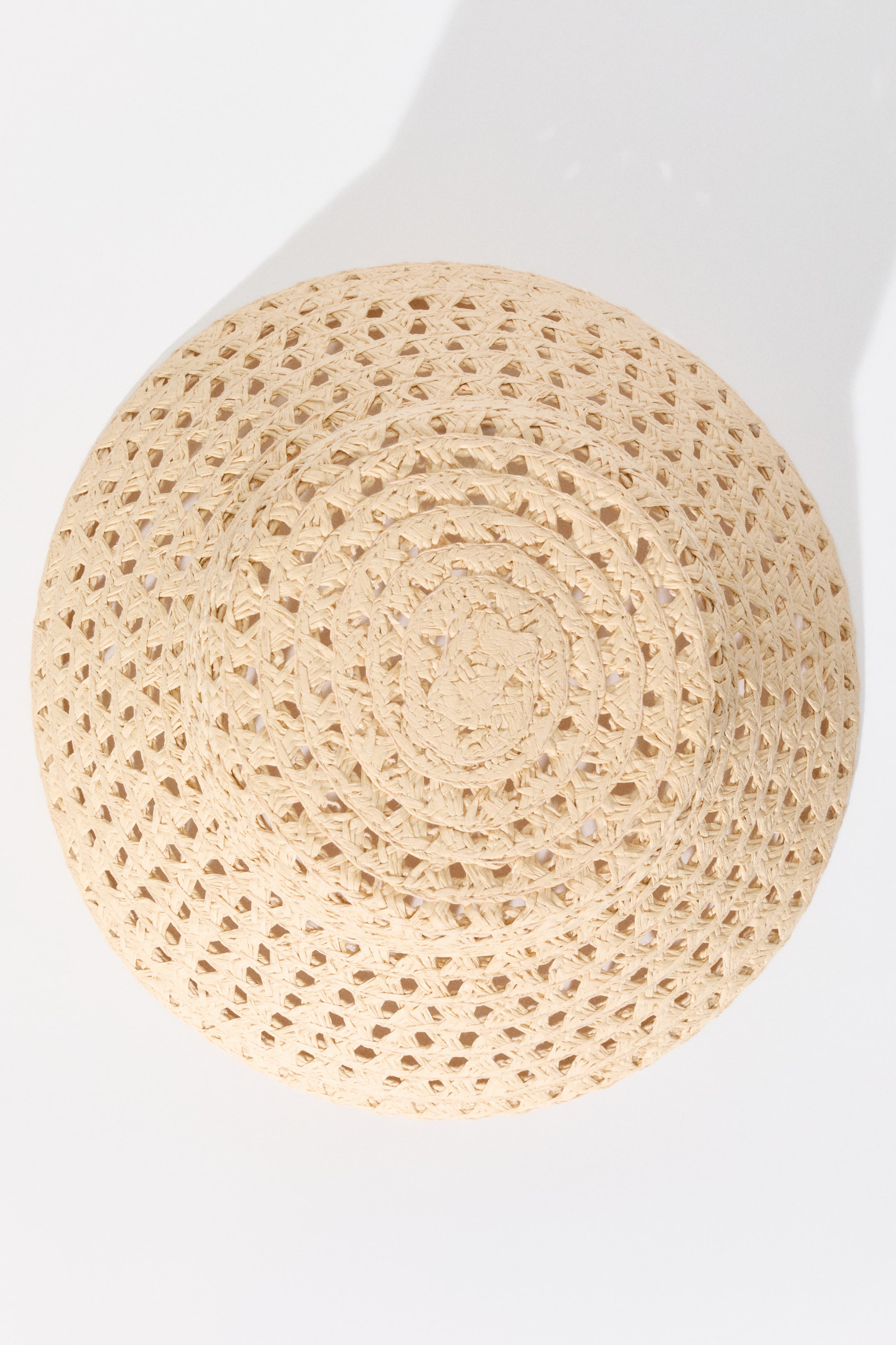 View larger image: A light beige straw hat showcases its circular open-weave pattern from a top-down view. The woven design creates small, evenly spaced openings across its surface.