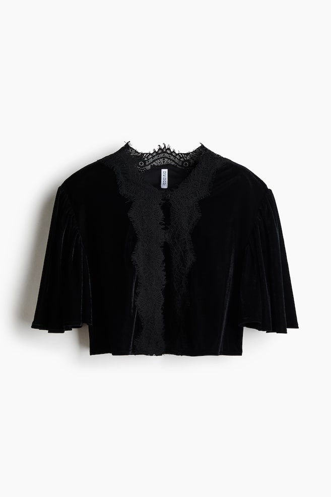 A black velvet cropped top is shown from the front, featuring a high lace-trimmed collar that extends into a decorative lace panel down the centre front. The top features wide, draped short sleeves and a straight cropped hem. - 1