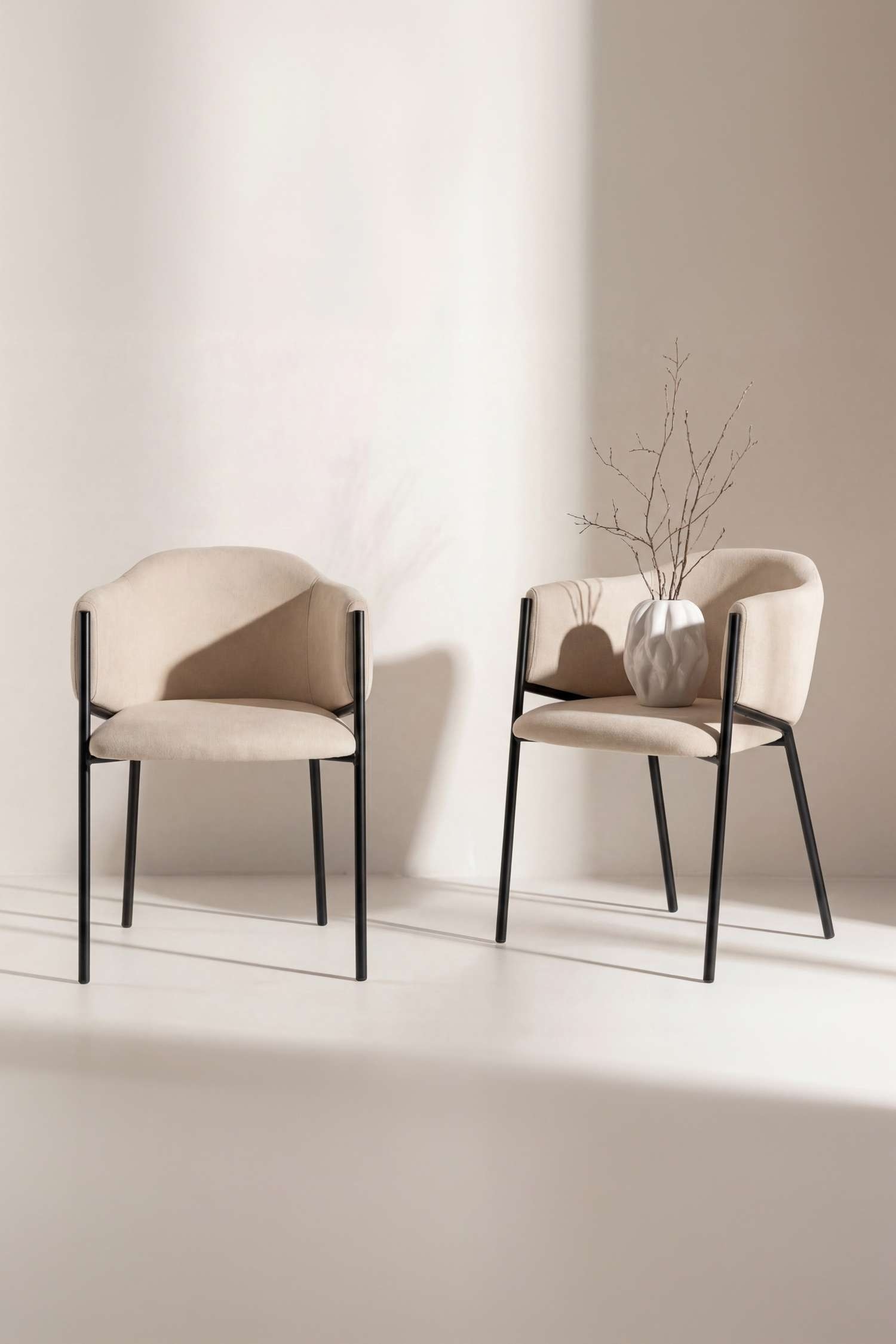 Una poltrona imbottita Ã¨ rivolta in avanti e presenta uno schienale curvo in tessuto beige con braccioli integrati inclinati e una seduta imbottita abbinata. La poltrona Ã¨ sorretta da una struttura in metallo nero con quattro gambe dritte e sottili che si estendono verso lâalto lungo i lati esterni dei braccioli.