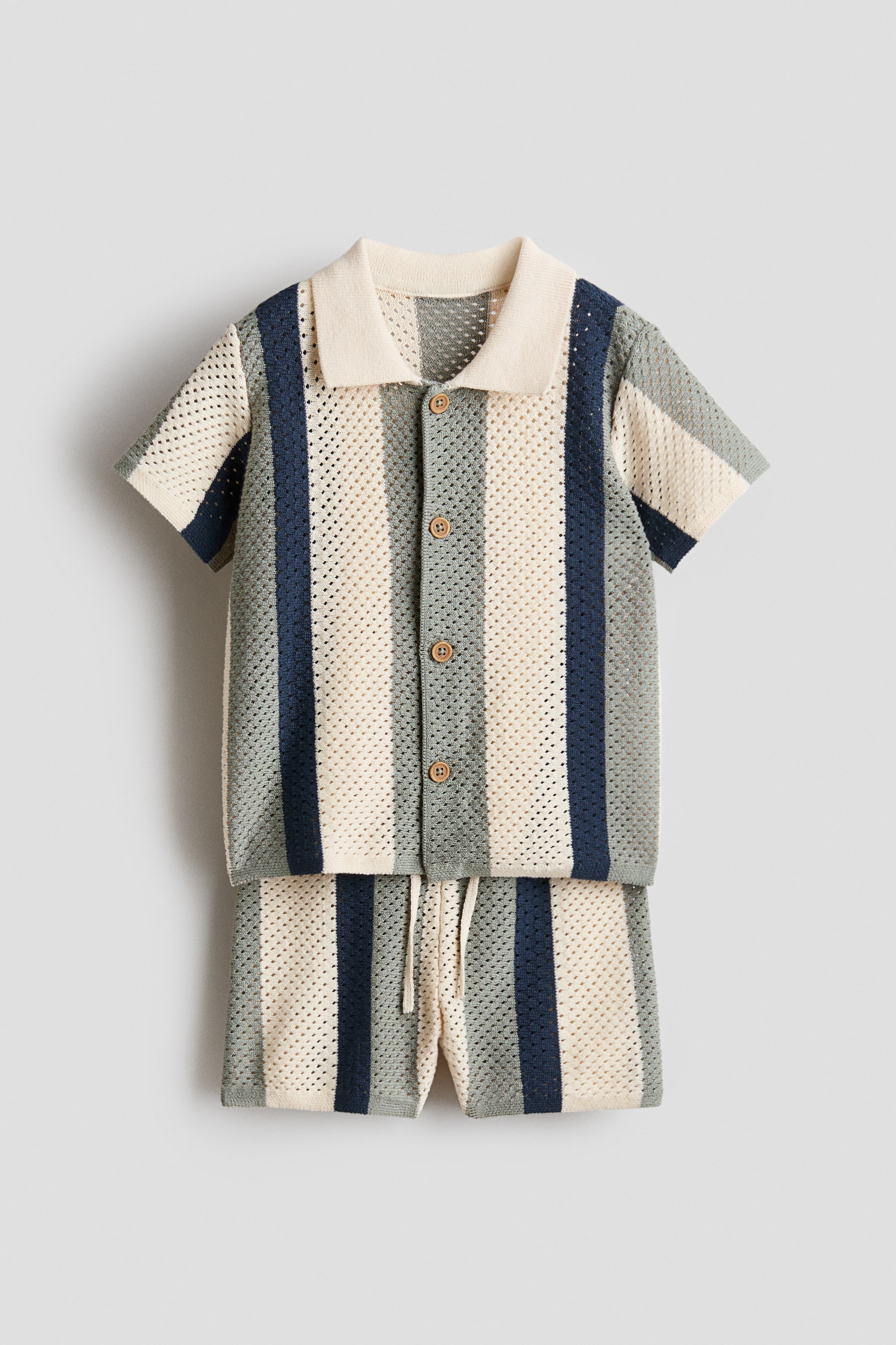 View larger image: A mesh-knit set — a short-sleeve shirt and matching shorts — shown from the front, featuring vertical stripes in cream, light green, and navy. The shirt has a ribbed collar, buttons down the front, and fine-knit trim at the cuffs and hem, while the shorts feature an elastic drawstring waist and fine-knit hems.