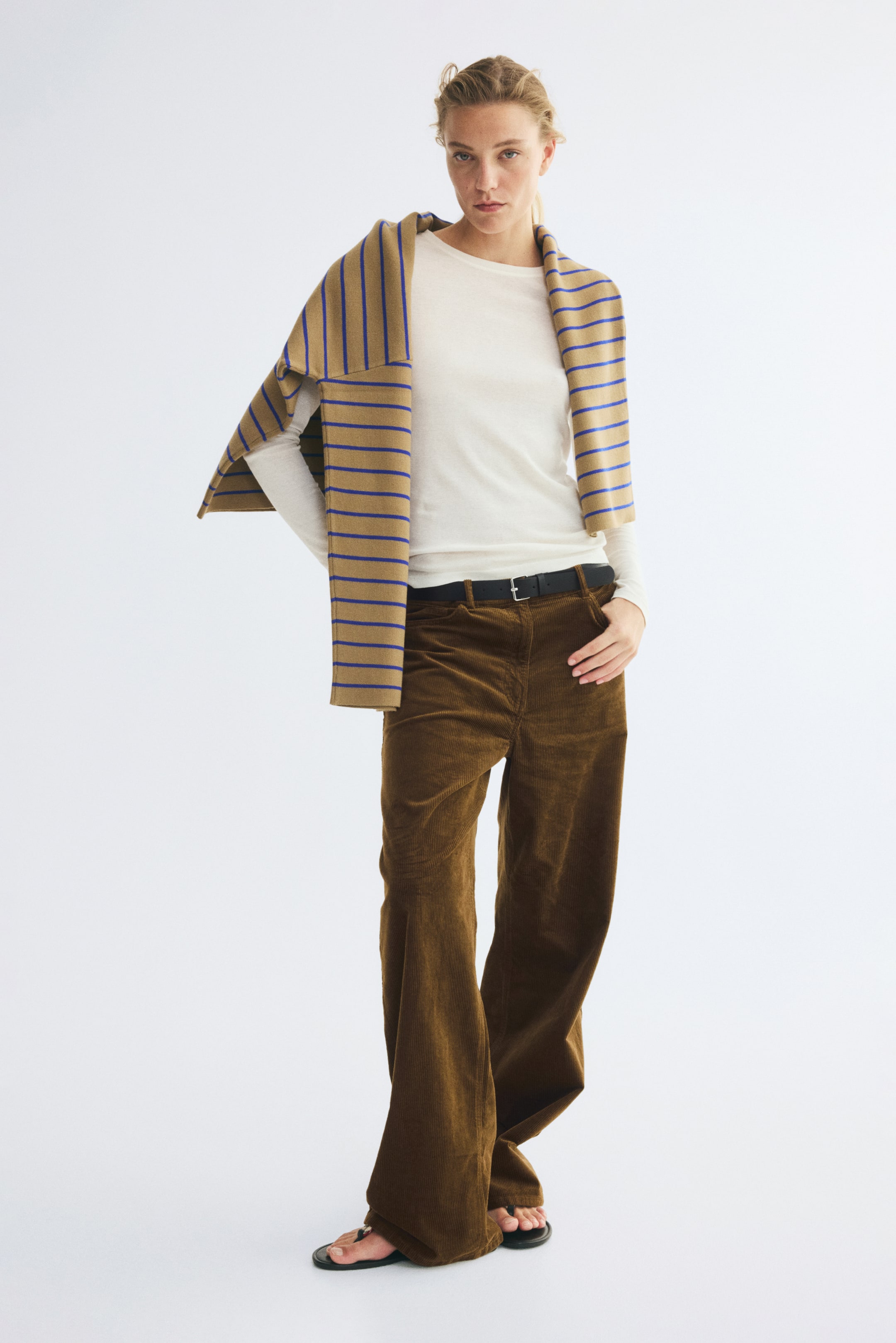 View larger image: High-waisted brown cotton corduroy pants are worn in a front-facing view, showcasing a straight-leg silhouette, front pockets, and a black belt with a silver buckle. A white long-sleeve top is tucked into the waistband to highlight the high-rise fit.