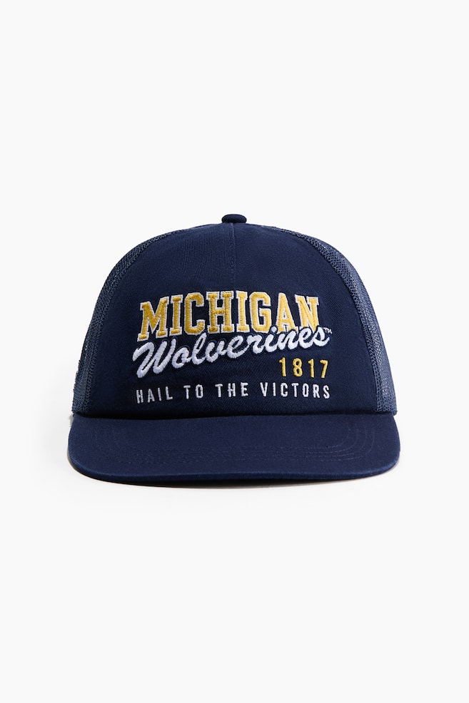 En marinblÃ¥ truckerkeps visas framifrÃ¥n och har en solid frontpanel, en platt skÃ¤rm och en matchande mesh-baksida. Frontpanelen pryds av broderad text som lyder "MICHIGAN" i gula blockbokstÃ¤ver, "Wolverines" i vit skrivstil, "1817" i gult och "HAIL TO THE VICTORS" i vitt. - 1