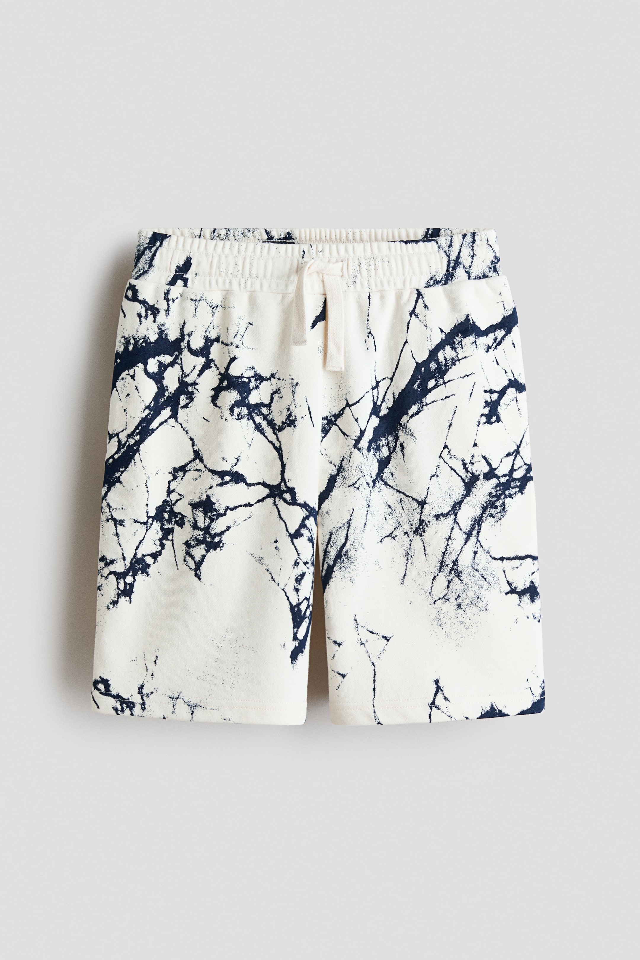 View larger image: The front of a pair of shorts showcases a white lightweight sweatshirt fabric adorned with a dark blue abstract print. It features an elasticated drawstring waist, fastened with a natural-colored tie, and raw-edge hems.
