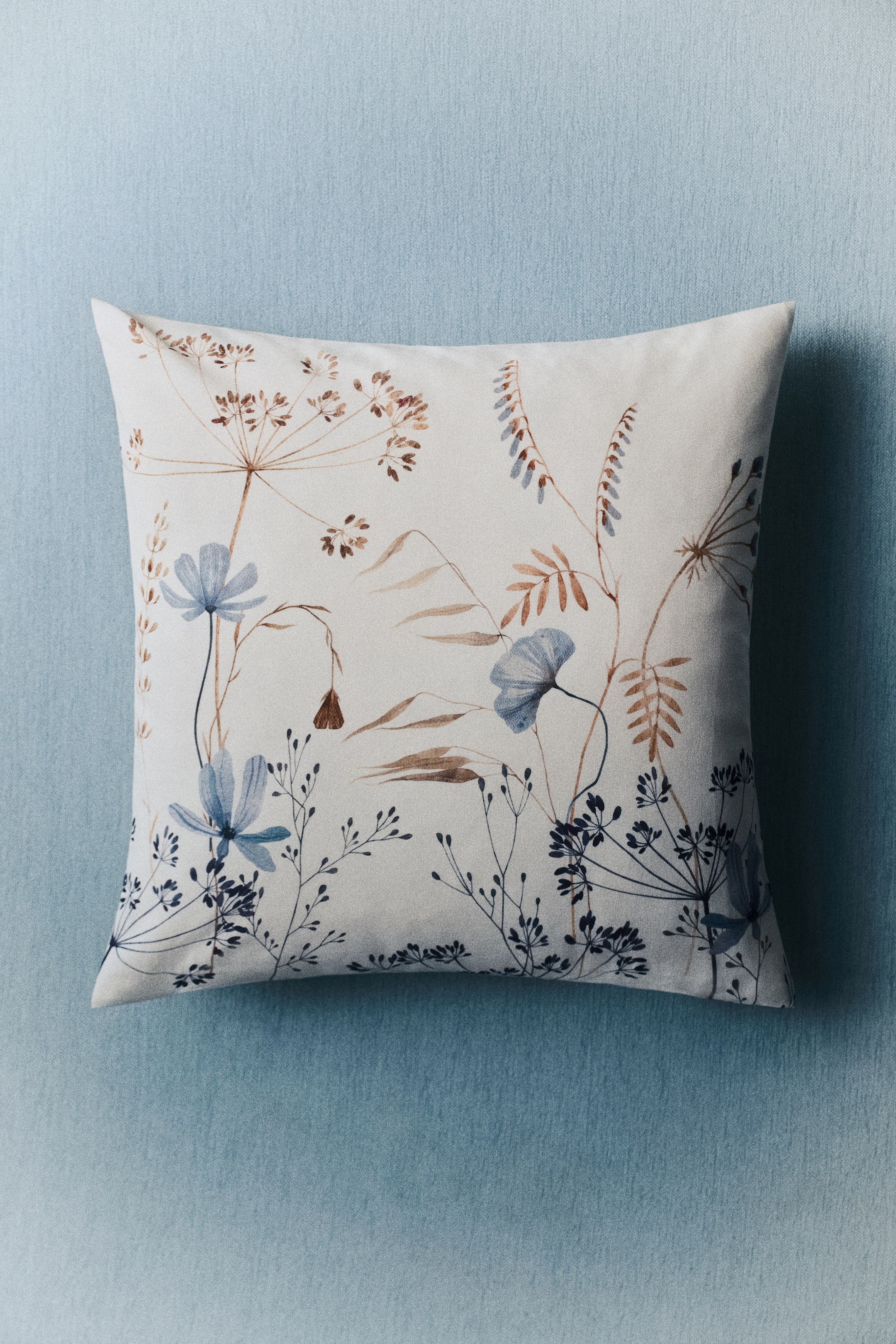 Grotere afbeelding bekijken: Een katoenen canvas kussenhoes toont zijn voorkant, met een botanische print. De print toont verschillende planten met blauwe bloemen, bruine zaadhoofden en donkerblauwe stelen op een gebroken witte achtergrond.