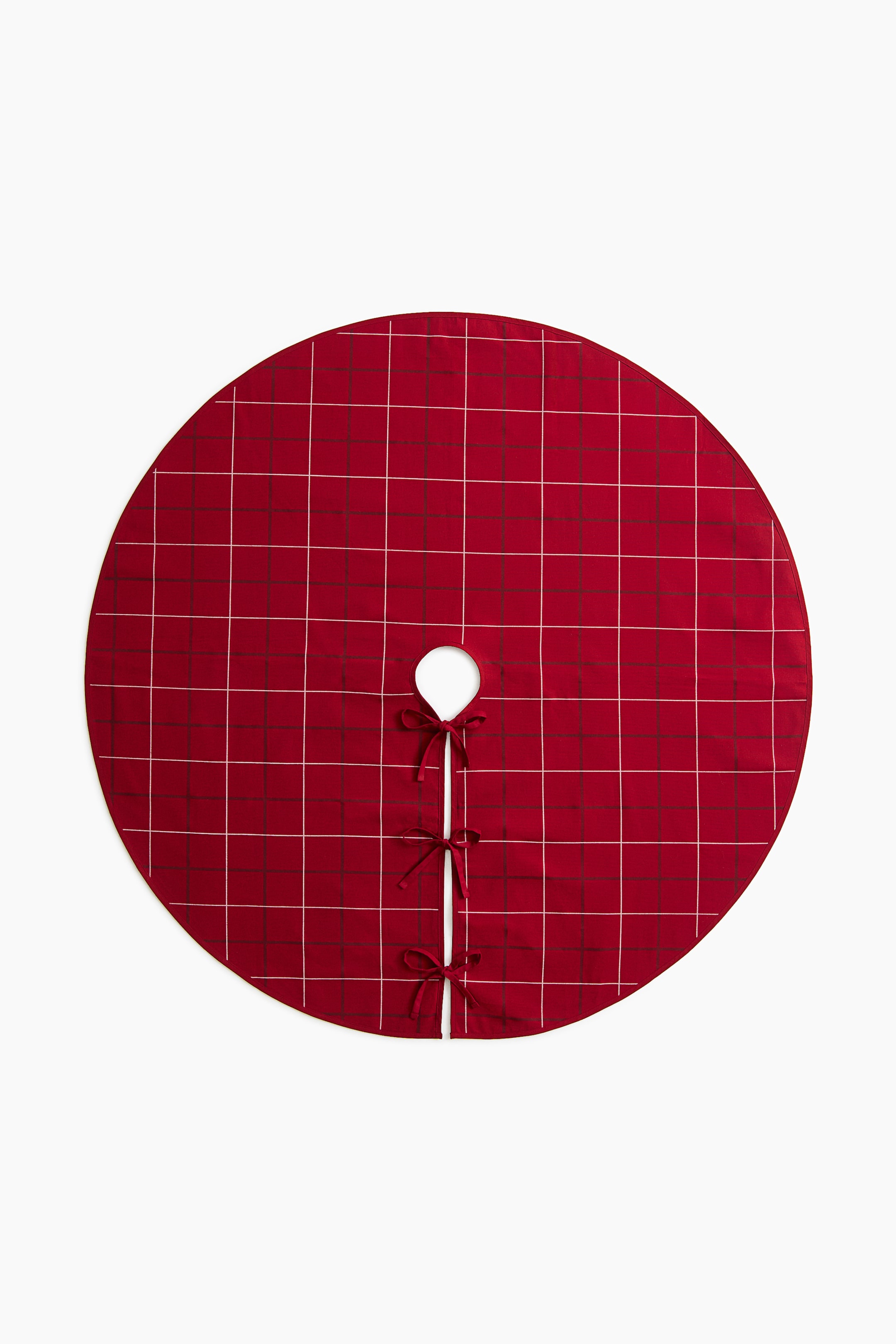 Visualizza immagine più grande: Un copribase per albero circolare è realizzato in tessuto rosso con un motivo a quadri finestra bianco. La vista frontale mostra un'apertura centrale circolare con un taglio diritto, fissato da tre lacci coordinati in tessuto rosso annodati a fiocco.