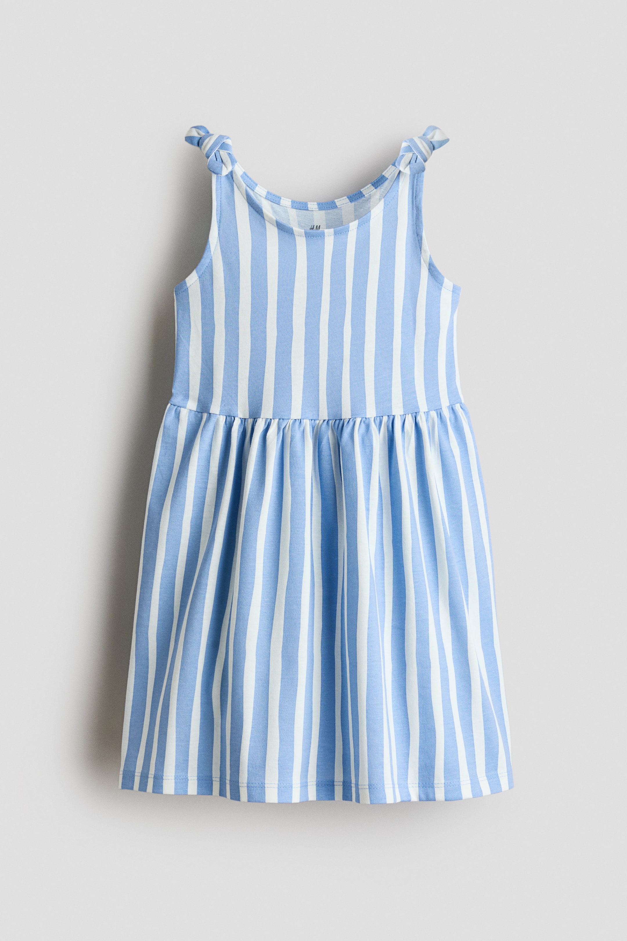 View larger image: The dress showcases blue and white vertical stripes, with shoulder straps tied in knots. A gathered seam defines the waist, leading to a flared skirt.