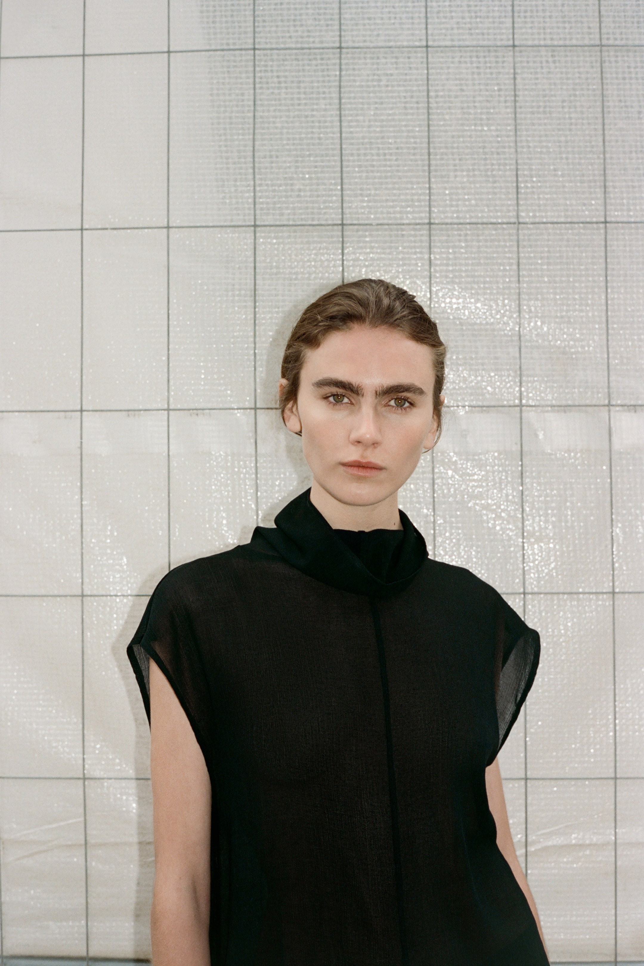 View larger image: The model is wearing a black sleeveless top with a high draped neckline and a visible vertical seam running down the center front.