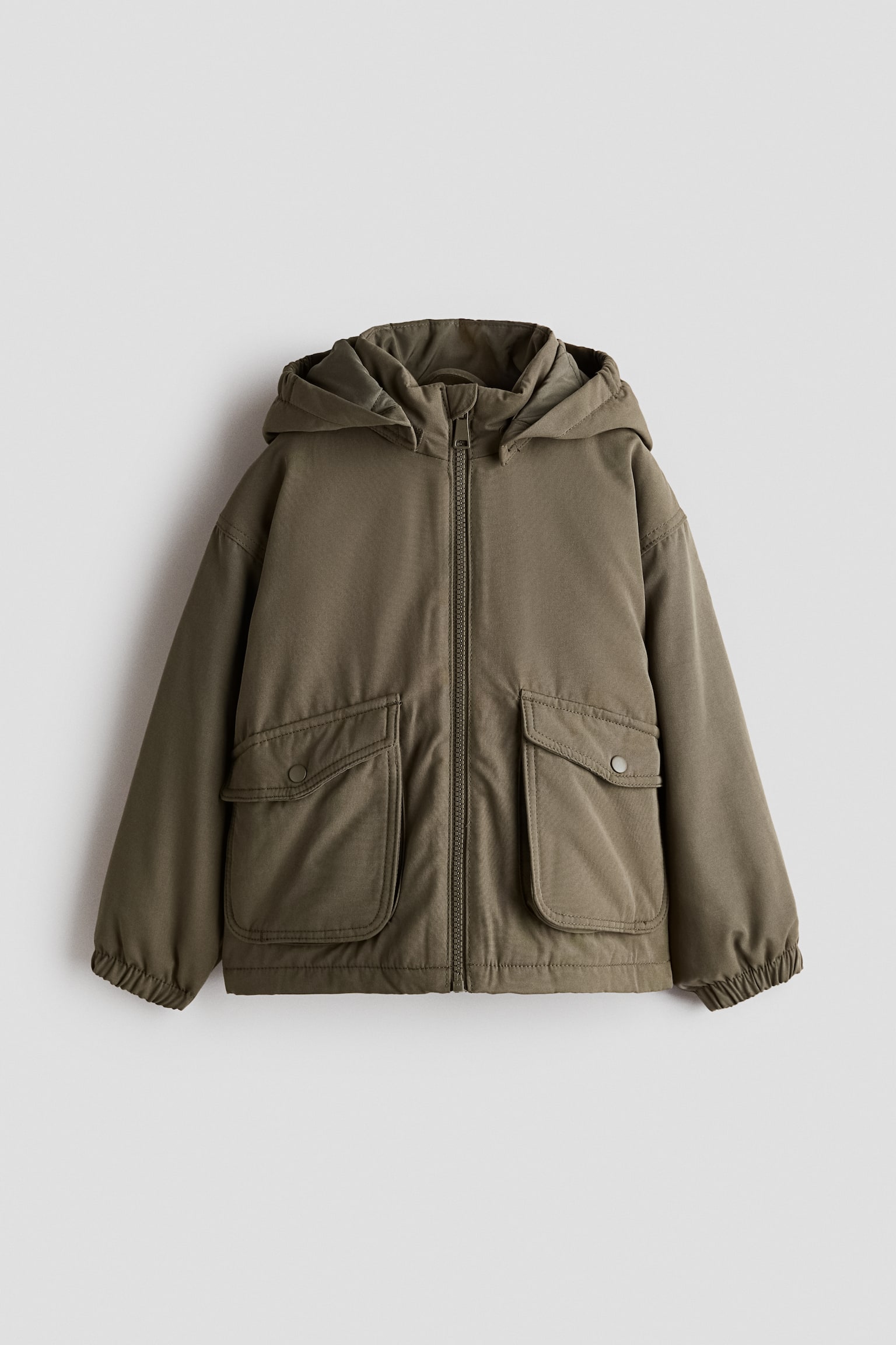 An olive-green, lightly padded jacket is shown from the front, featuring a zip closure, an attached hood, and dropped shoulders. It showcases two large bellows pockets with snap-button flaps and long sleeves with elasticated cuffs.