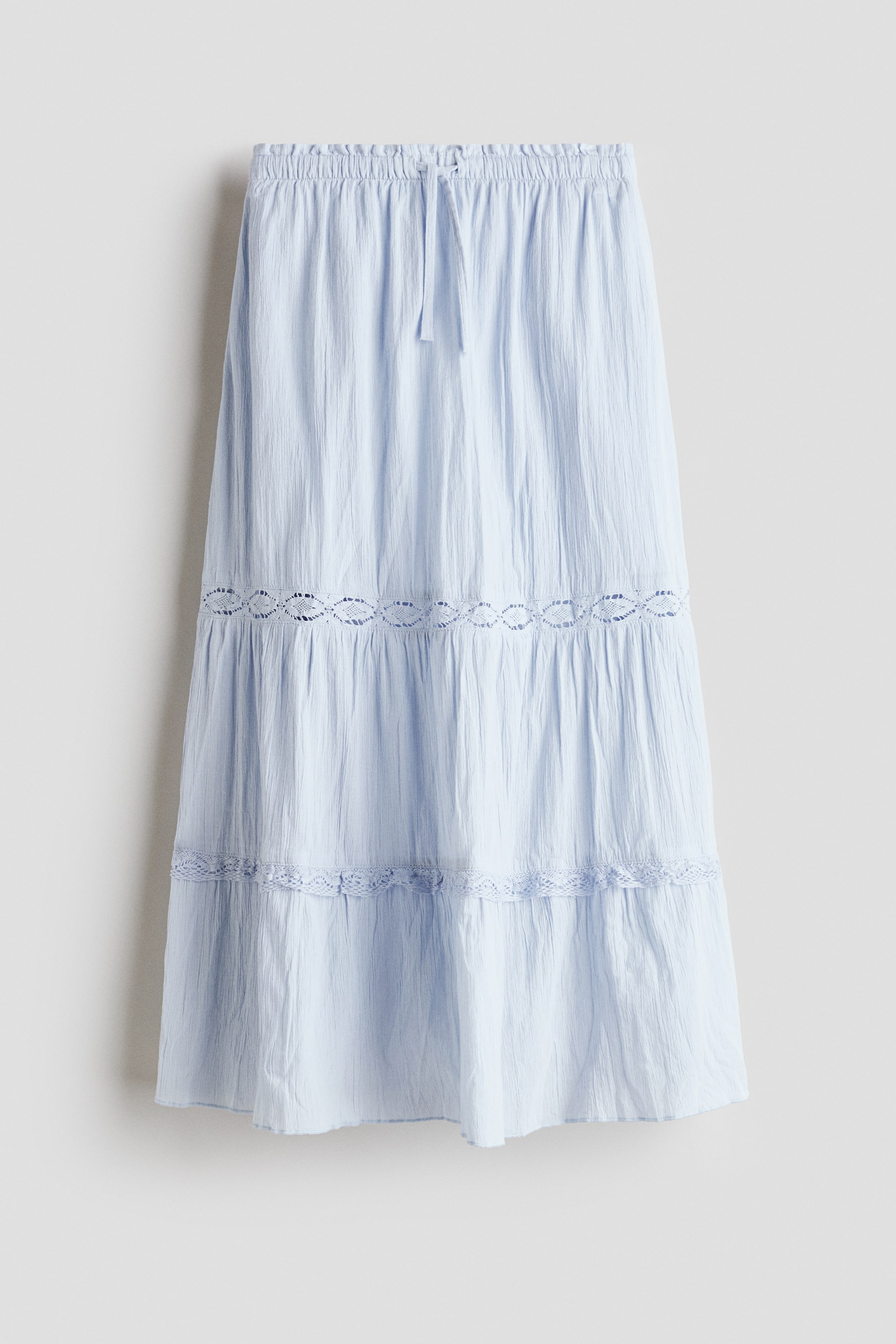 View larger image: A light blue tiered skirt is shown from the front, featuring a shirred waistband with a drawstring tie. It displays three gathered tiers, with a wide openwork lace trim joining the first two tiers and a narrower lace trim joining the second and third tiers.