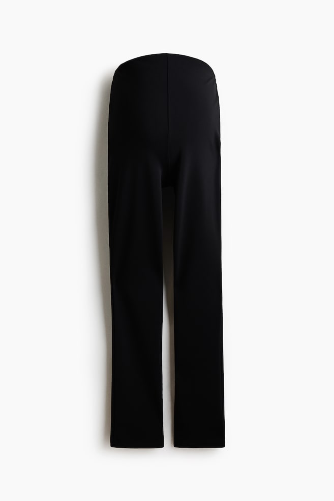 Schwarze gerade geschnittene Hosen hängen gerade herab und verfügen über einen hohen, nahtlosen Bund sowie ein klares, minimalistisches Design mit einer Mittelnaht. Die Hosen präsentieren einen glatten, matten Stoff mit strukturiertem Fall und gerade geschnittenen Hosenbeinen. - 1
