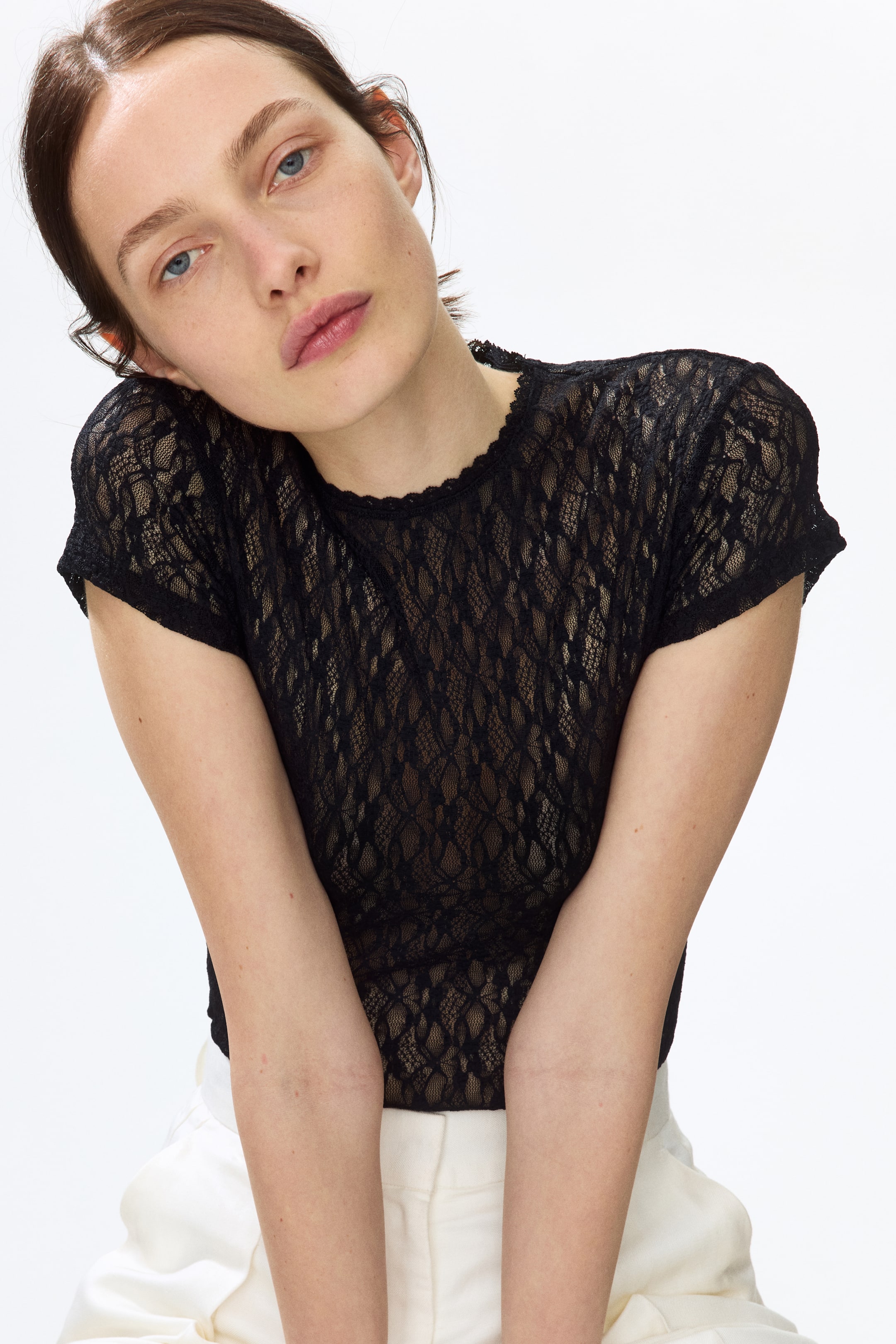 View larger image: The model is showcasing a black thong bodysuit crafted from lace-look jersey, featuring a round neckline and short sleeves, paired with light-coloured trousers.