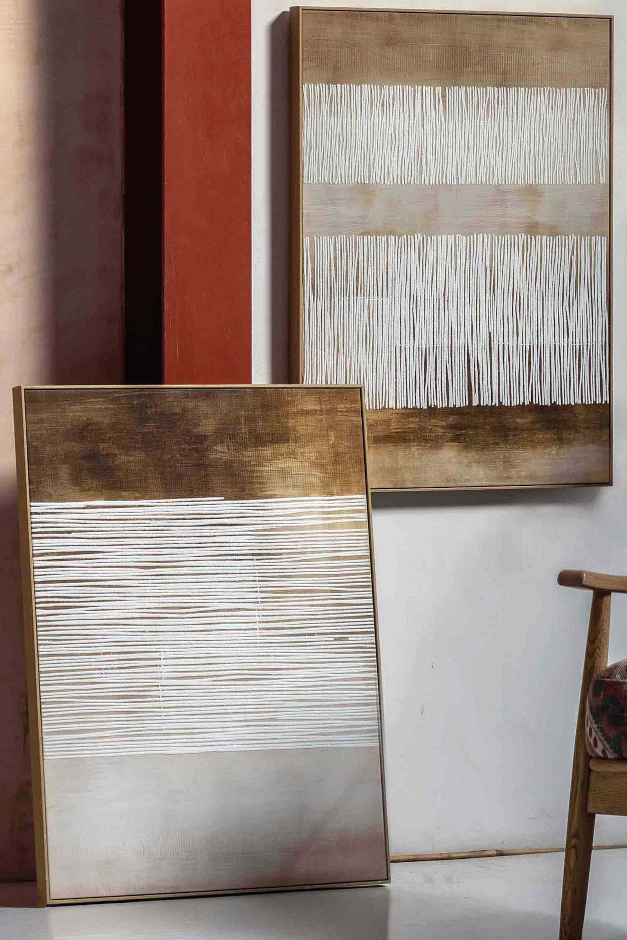 View larger image: A rectangular framed abstract artwork is leaning forward, presenting a design with three horizontal bands. The top band is dark brown with a brushed texture, the middle band features numerous white horizontal textured lines over a light brown background, and the bottom band is light beige, all enclosed by a thin gold-coloured frame.