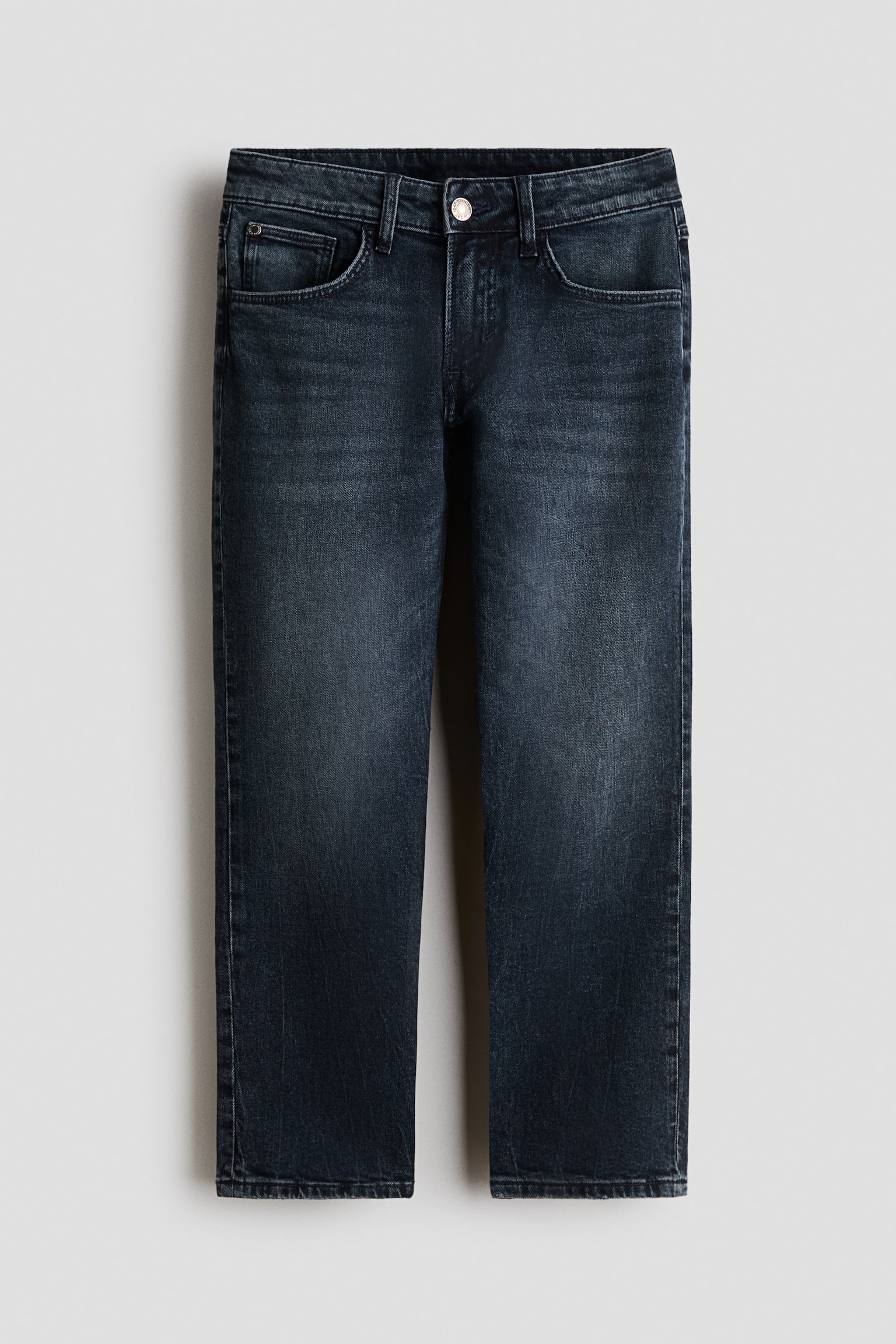 Para ciemnych jeansów denim w stylu five-pocket jest prezentowana od przodu, z luźnym krojem i zwężanymi nogawkami. Jeansy mają subtelne sprania na udach i kolanach, a także pasek z szlufkami na pasek oraz metalowe zapięcie na guzik.