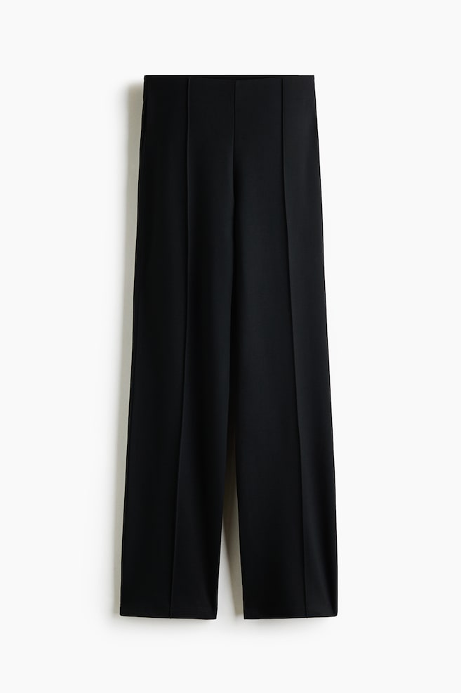 Schwarze Hose aus Ponte-di-Roma-Jersey, von vorne gezeigt, mit hohem Bund und verdecktem, elastischem Bund. Das Design prÃ¤sentiert eine schmale Passform mit markanten, genÃ¤hten BÃ¼gelfalten, die mittig entlang jedes Hosenbeins verlaufen und zum Saum hin in einen leichten Schlag auslaufen. - 1