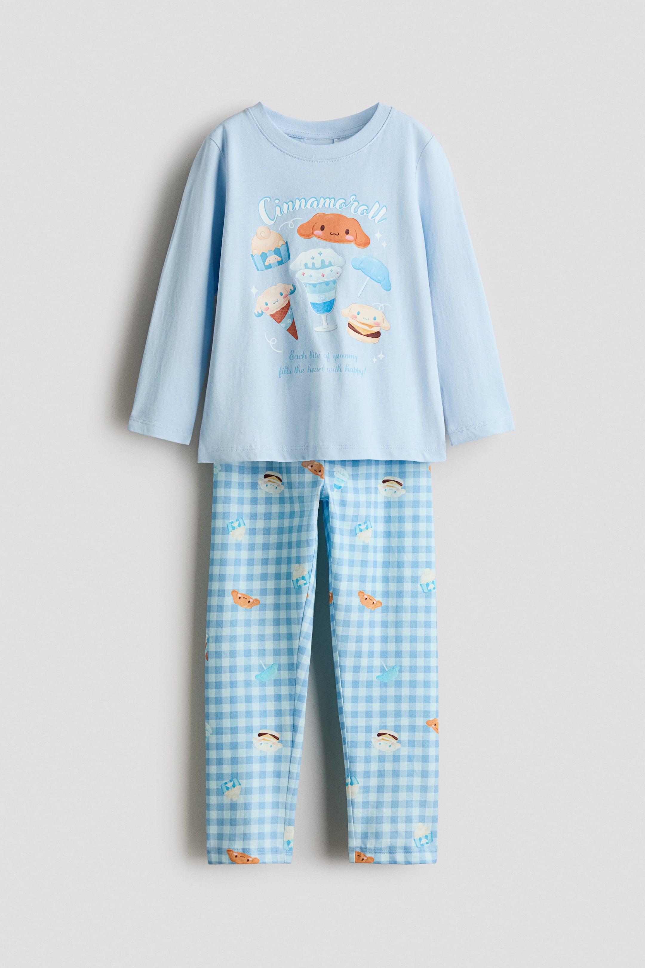 View larger image: A pyjama set is shown from the front, featuring a light blue long-sleeved top with a round, rib-trimmed neckline and a Cinnamoroll graphic on the chest. The matching pants are displayed in a light blue and white gingham pattern with a scattered character print.