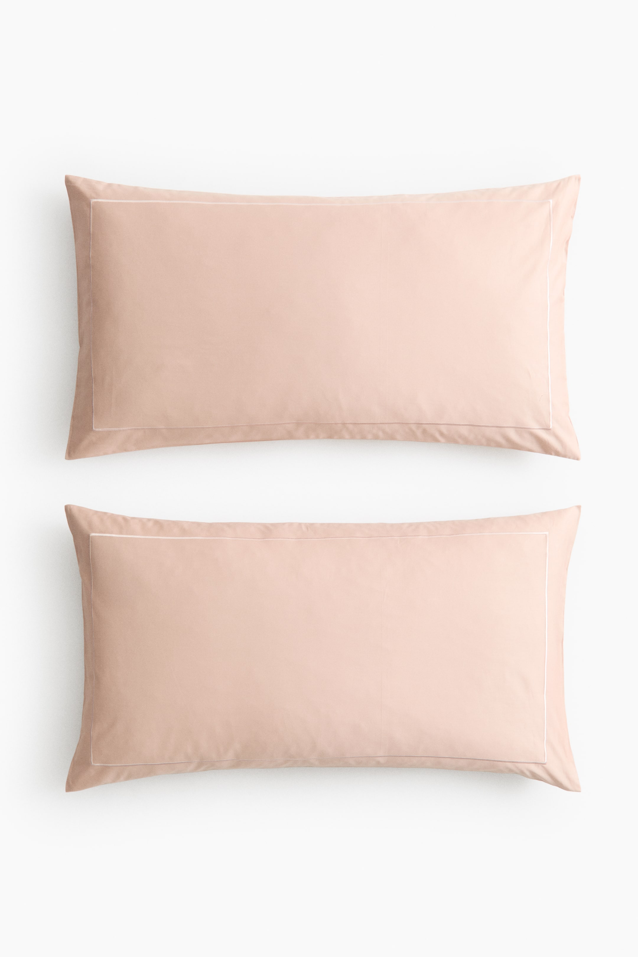 View larger image: Two rectangular pillowcases are displayed with their front sides facing up, lying flat. Each pillowcase is a soft peach colour and features a delicate white embroidered border outlining its perimeter, positioned slightly inward from the edges.
