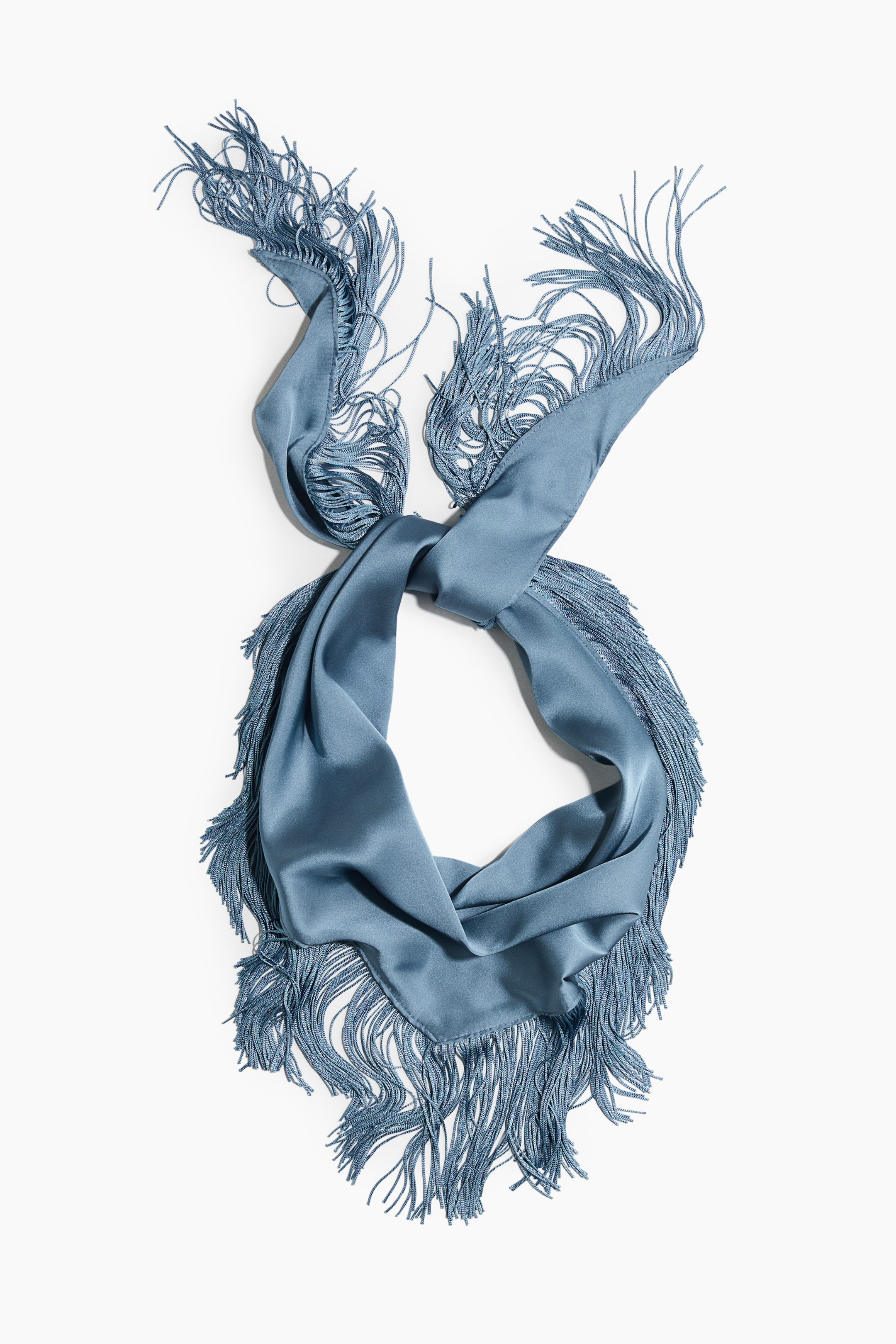 Visualizza l'immagine ingrandita: Un foulard triangolare blu è composto da un raso che cade morbidamente e presenta lunghe frange lungo due bordi. È esposto da un'angolazione dall'alto verso il basso, con il suo centro che forma un nodo e crea due anelli prominenti.