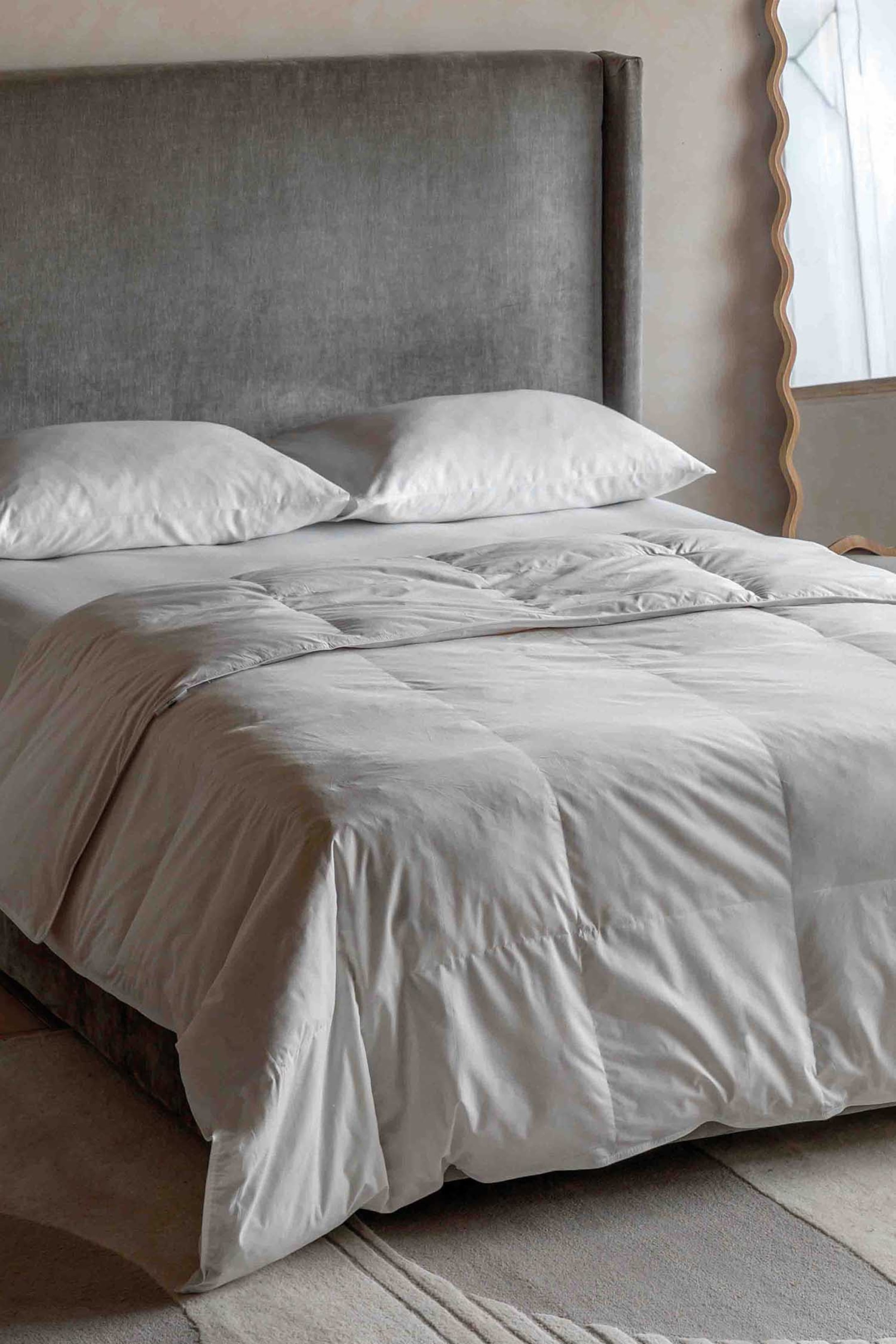 View larger image: A white duvet with visible square baffle box stitching is covering a bed, with a section folded back revealing its plush thickness. Two white pillows are resting at the head of the bed.