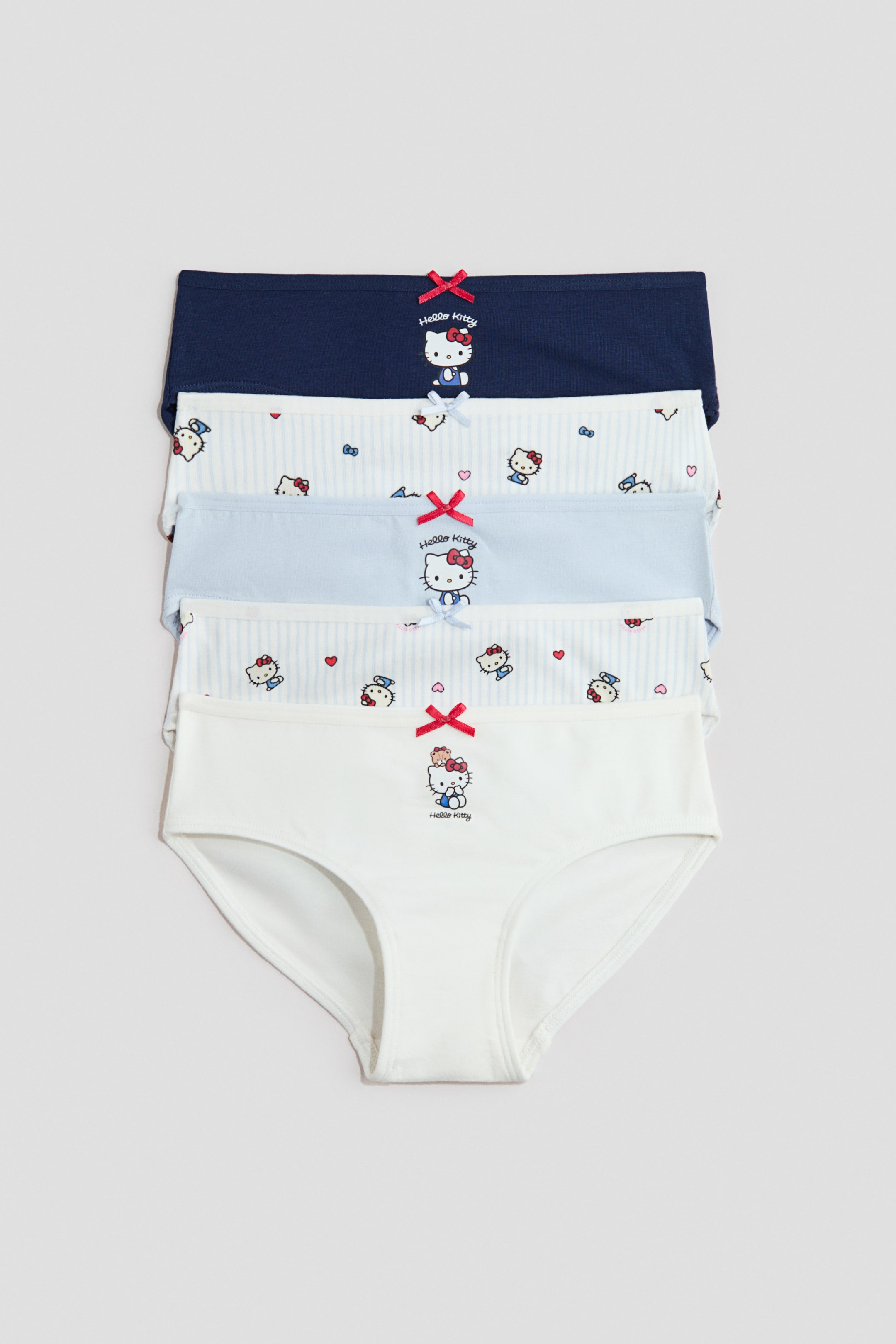 View larger image: Five pairs of briefs are neatly stacked, displaying their front. They feature soft, printed cotton jersey, each with an elasticated waistband and a small decorative satin bow at the front. Designs include Hello Kitty motifs, stripes, and solid colours in shades of blue and white.