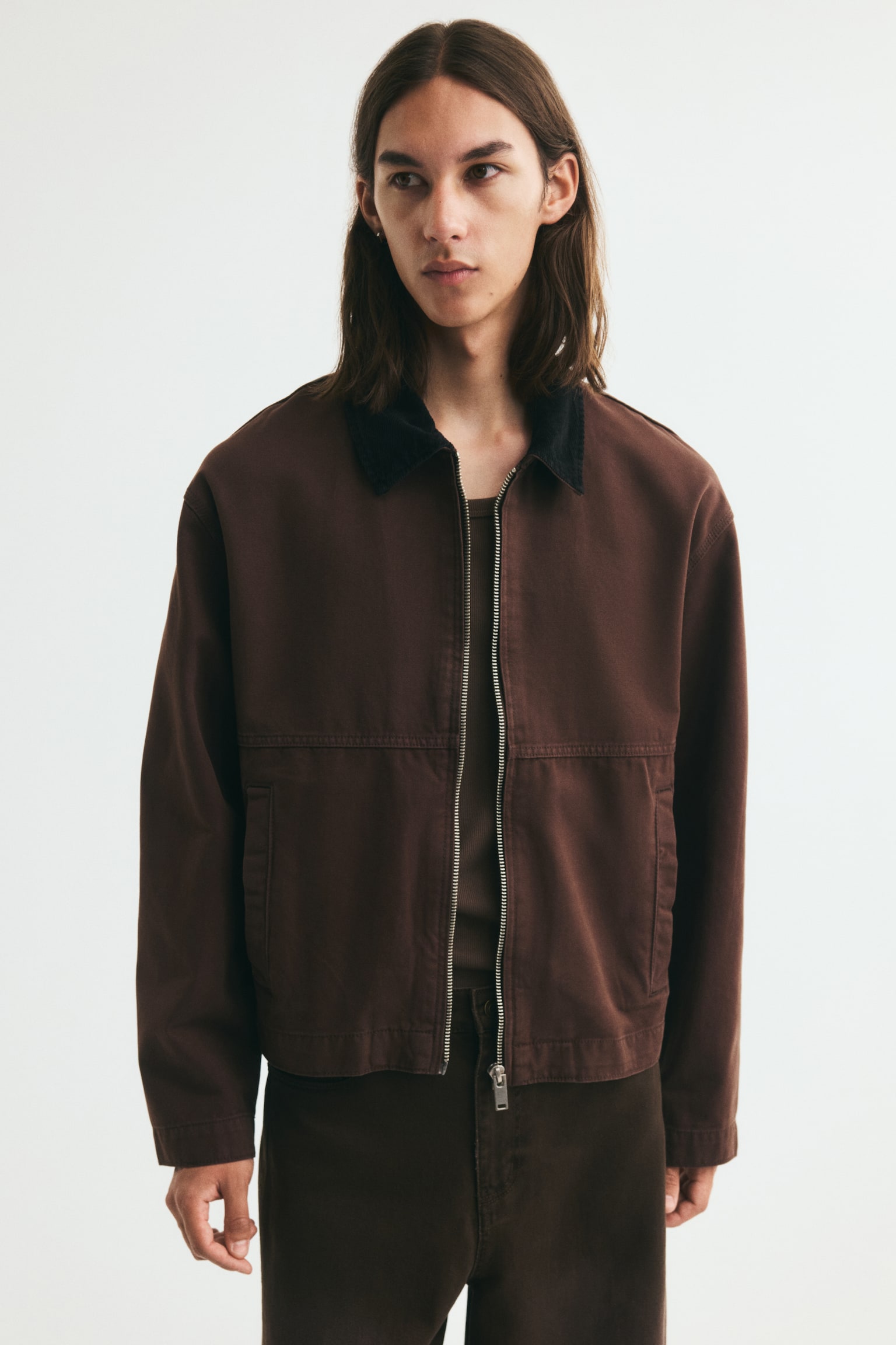 A short workwear jacket in brown cotton canvas is showcased from the front, featuring a contrasting black corduroy collar. A silver-toned zip runs down the front, with two welt front pockets, long sleeves, and a straight-cut hem completing the design. - 1