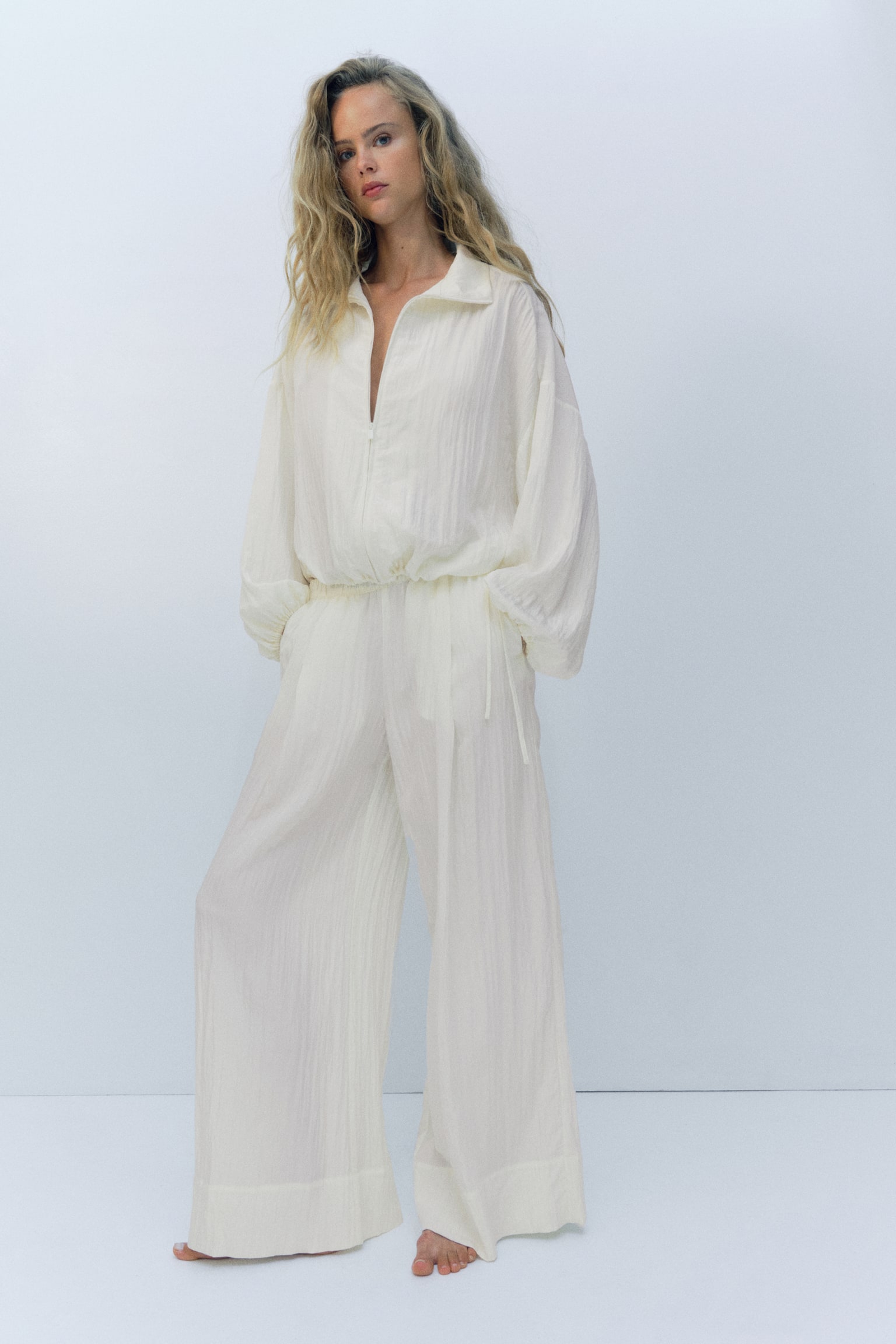 Cream wide-leg trousers featuring a crinkled texture, an elasticated waistband, and a visible side pocket, with a cropped length, presented flat-lay and front-facing. - 1