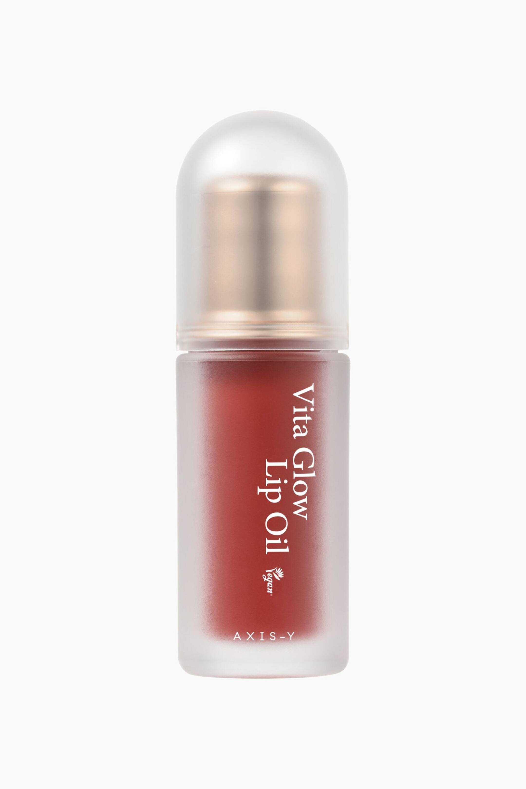 Visa större bild: En cylindrisk lip oil-flaska står upprätt och vänd framåt. Flaskan och dess rundade kork har en frostad, halvtransparent finish, med en metallisk bronstonad komponent synlig under korken. En rödbrun lip oil fyller flaskan, och "Vita Glow Lip Oil" är tryckt vertikalt på sidan, tillsammans med en "vegan"-logotyp och "AXIS-Y" längst ned.