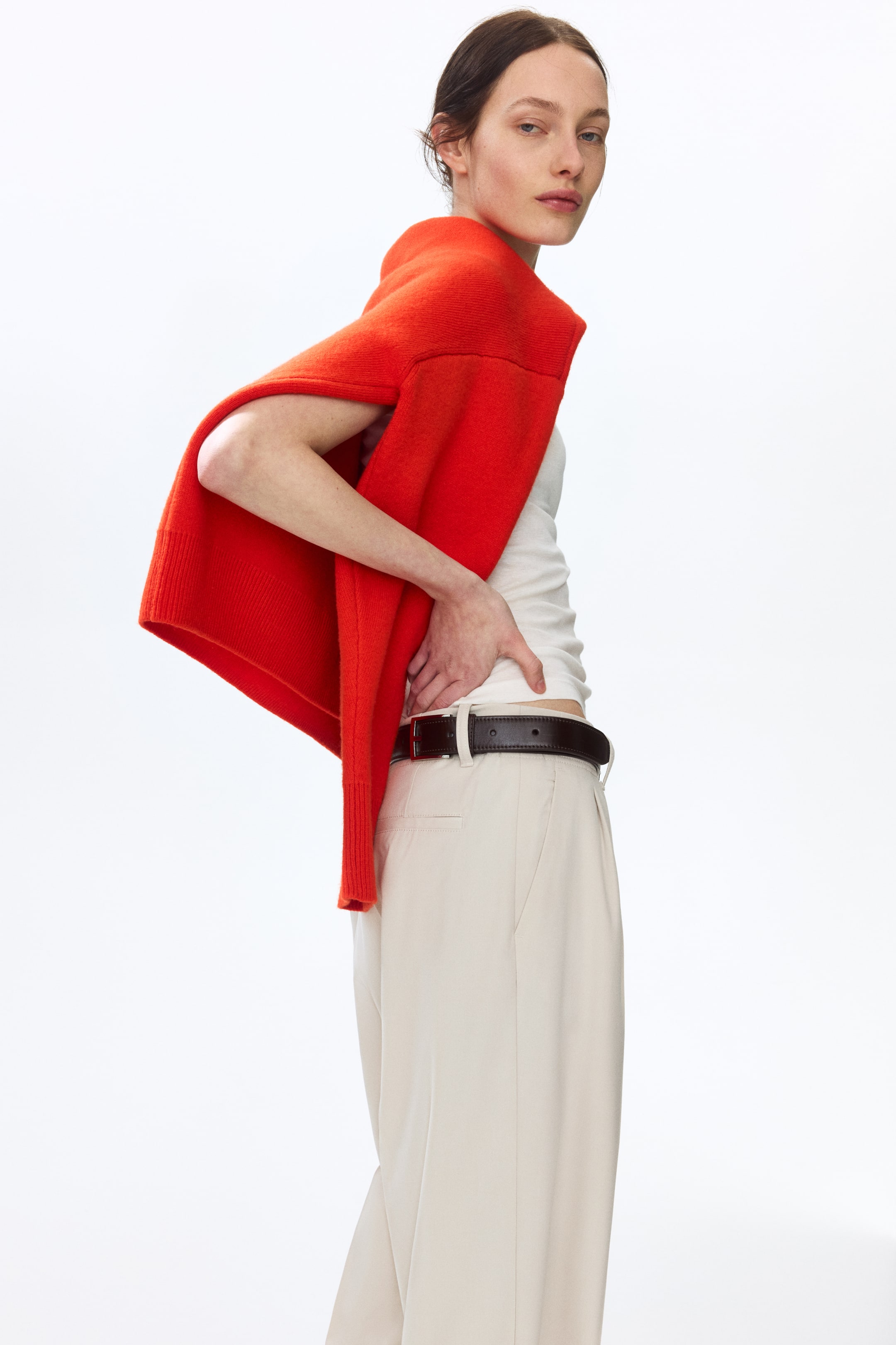 Voir une image plus grande: Le mannequin porte un pantalon beige clair à coupe ample, avec des poches latérales en diagonale, une poche arrière passepoilée partiellement visible, des plis à l'avant et des plis visibles le long des jambes droites. Une ceinture foncée est portée à travers la ceinture régulière, et le mannequin place ses mains sur le bas de son dos.