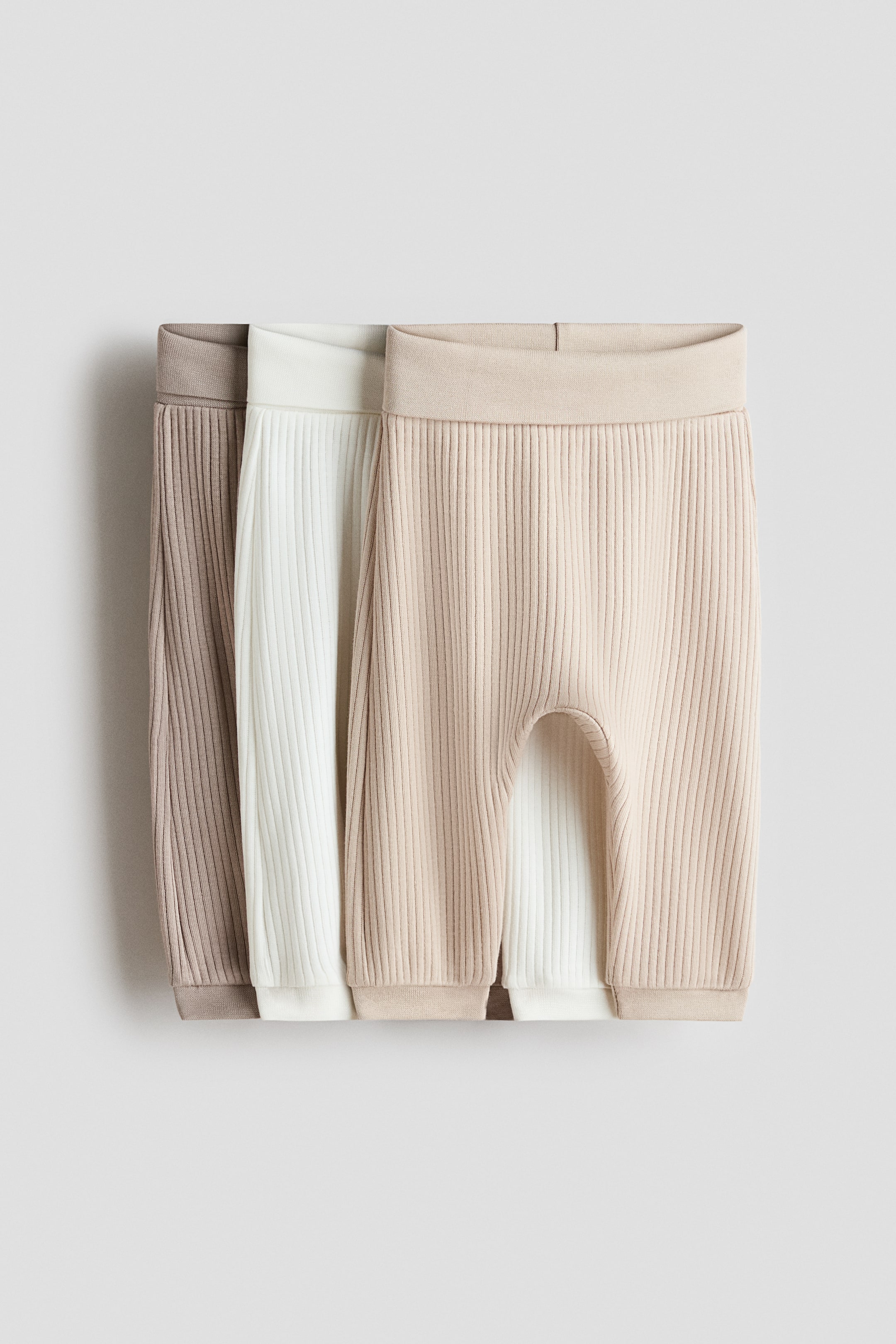 Ingrandisci l'immagine: Tre paia di pantaloni in maglia a coste sono presentati frontalmente, con vita elasticizzata e polsini alla caviglia a coste, nei colori taupe chiaro, avorio e beige chiaro.