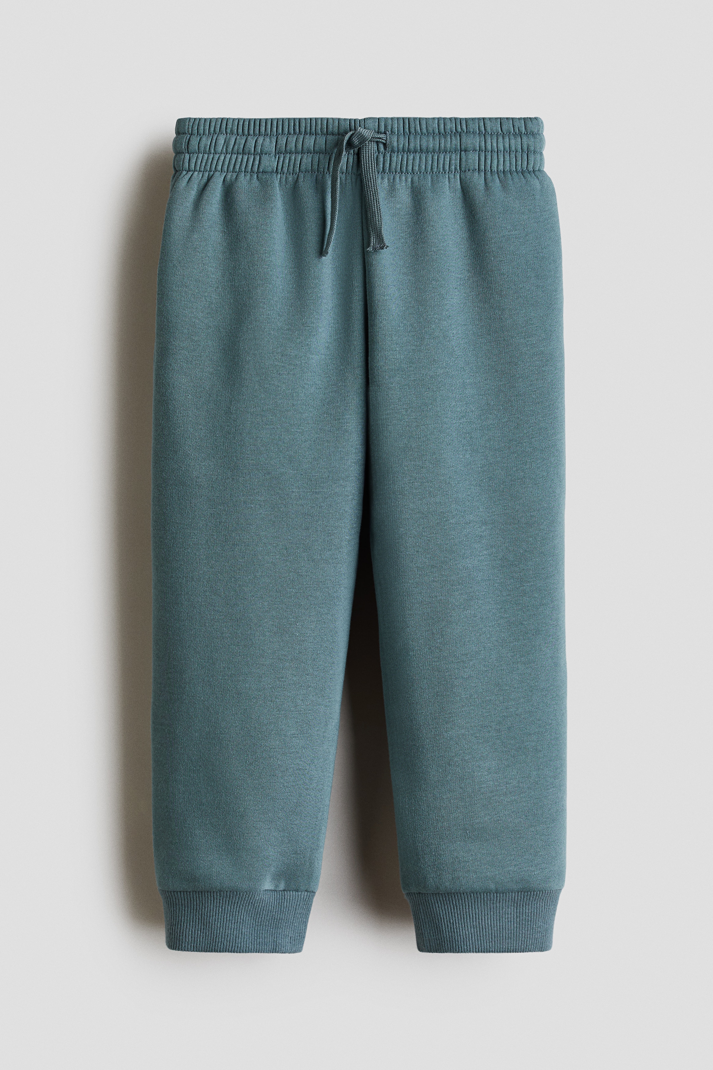 Mavi-gri sweat kumaÅÄ±ndan, paÃ§alarda ribanalÄ± manÅetlere sahip, rahat kesim eÅofman altÄ±nÄ±n Ã¶nden gÃ¶rÃ¼nÃ¼mÃ¼. EÅofman altÄ±, uyumlu bir bisiklet yaka sweatshirt ve krem rengi spor ayakkabÄ±larla set halinde kombinlenmiÅtir.