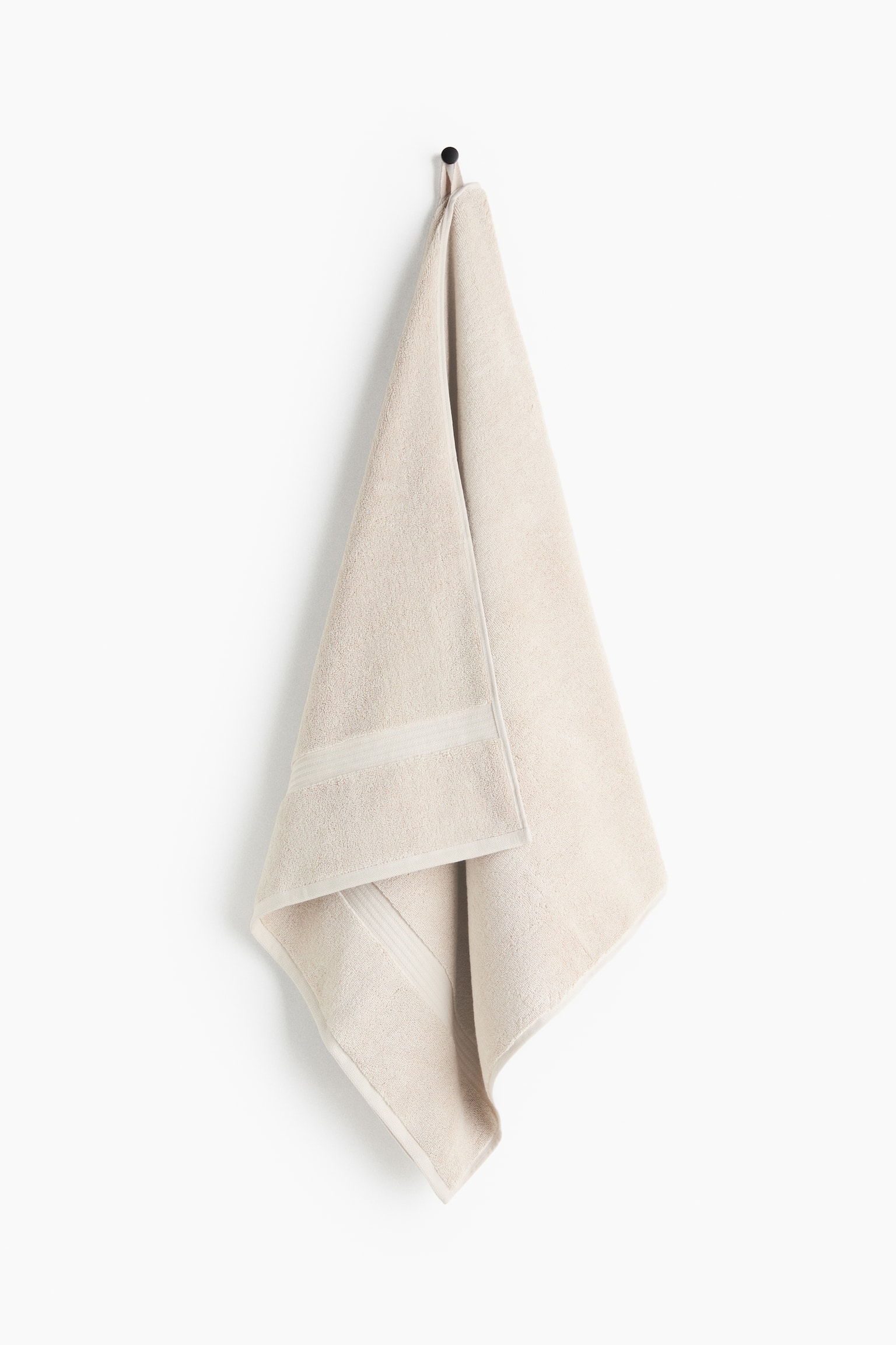 A light beige towel is hanging, folded, and displaying its soft, textured surface. A smoother, horizontal band is visible across the lower portion of the visible top fold, and its edges are neatly hemmed. - 1