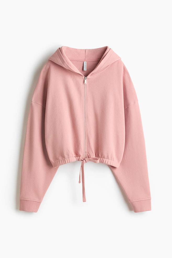 Eine pinke Kapuzenjacke wird von vorne gezeigt und verfügt über einen durchgehenden Reißverschluss sowie eine angenähte Kapuze. Sie hat lange Ärmel mit Rippbündchen und einen verkürzten Saum, der mittig vorne durch einen Kordelzug gerafft und zusammengebunden ist. - 1