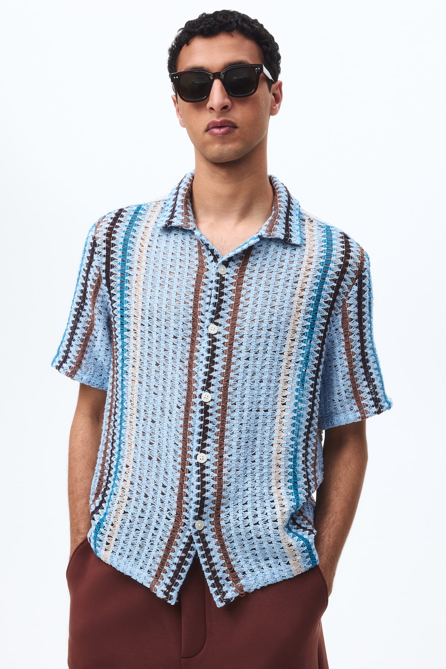 Short-sleeve shirt showcasing a crocheted design with vertical stripes in light blue, dark blue, brown, and beige hues. Features a classic collar and front button closure with white buttons. - 1