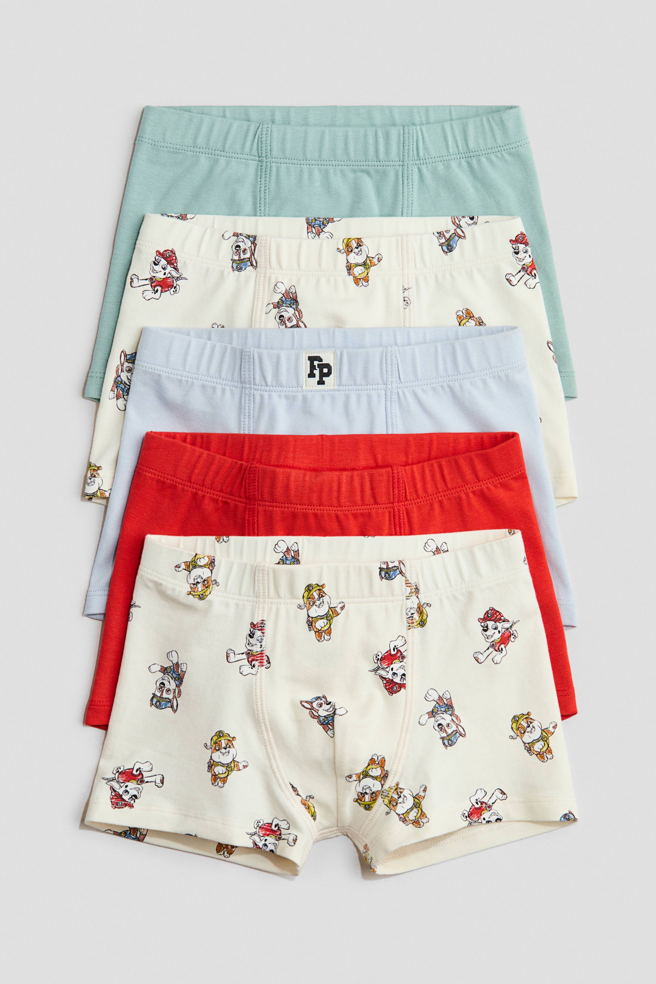 View larger image: A set of five cotton jersey trunks is displayed from the front, stacked with varying levels of visibility. Each trunk features a covered elastic waistband, short legs and a lined front panel. The set includes trunks in solid light green, solid red, solid light blue with an "FP" logo on the waistband, and two cream pairs with a repeating pattern of cartoon dog characters.