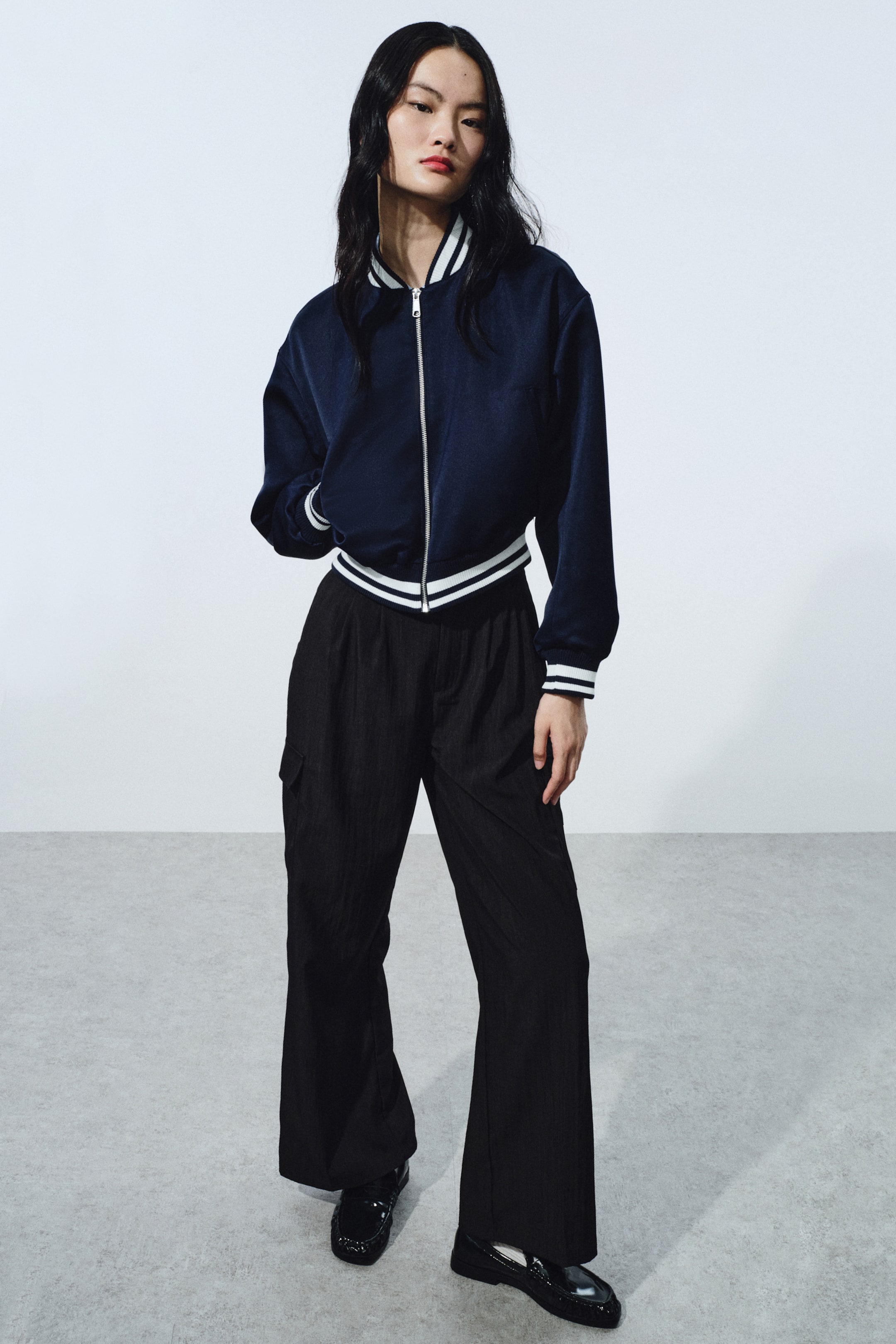 View larger image: A navy-blue bomber jacket features a full-zip front, a ribbed stand-up collar, and ribbed cuffs and hem detailed with white stripes. It fits loosely and sits at the waist.