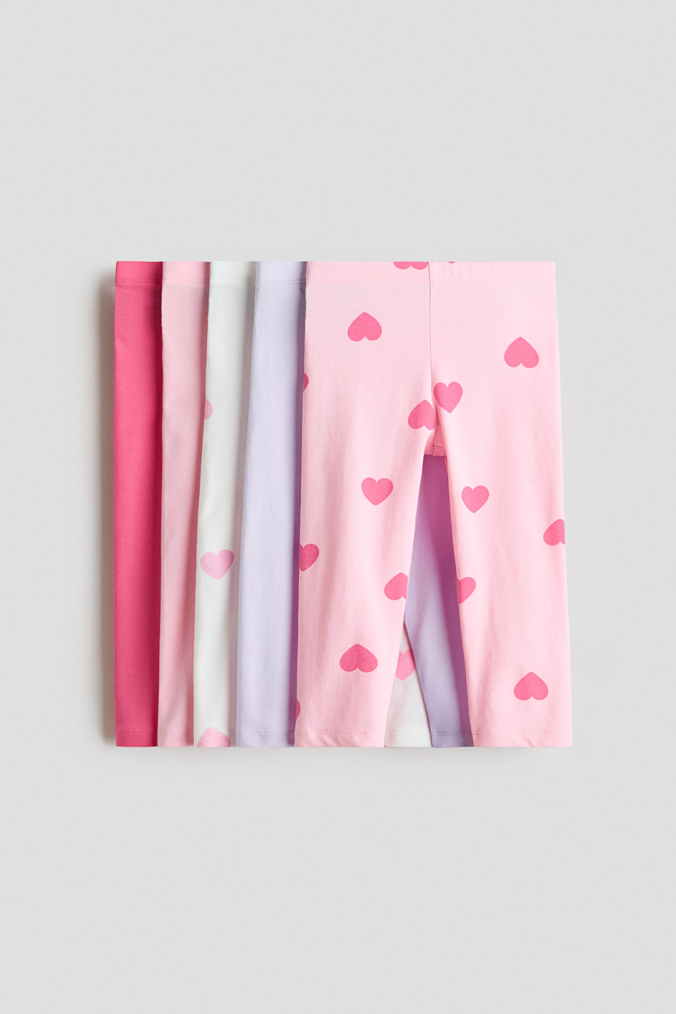 Größeres Bild anzeigen: 3/4-lange Leggings aus weichem Baumwolljersey mit verdecktem Gummizug in der Taille sind gestapelt und zeigen ihre Vorderansichten in einer Vielzahl von Farben. Diese Farben umfassen ein kräftiges Tiefrosa, Hellrosa, Weiß, Lavendel und ein hellrosa Paar mit fuchsiafarbenen Herzmustern.