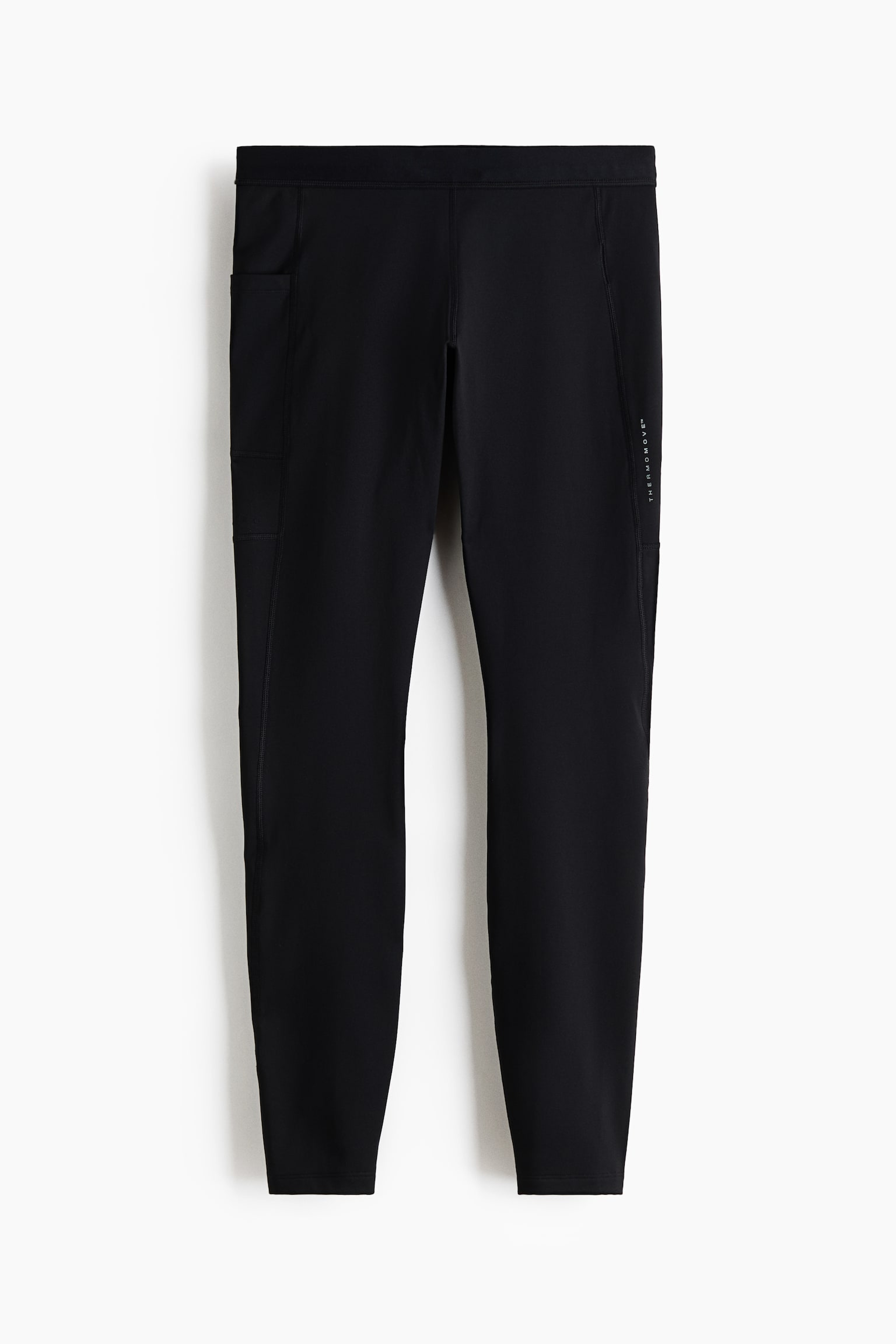 A pair of black athletic leggings is shown from the front, featuring a wide elastic waistband and flatlock seams. The leggings include a deep side slip pocket on the right leg and a small vertical text graphic on the left leg.