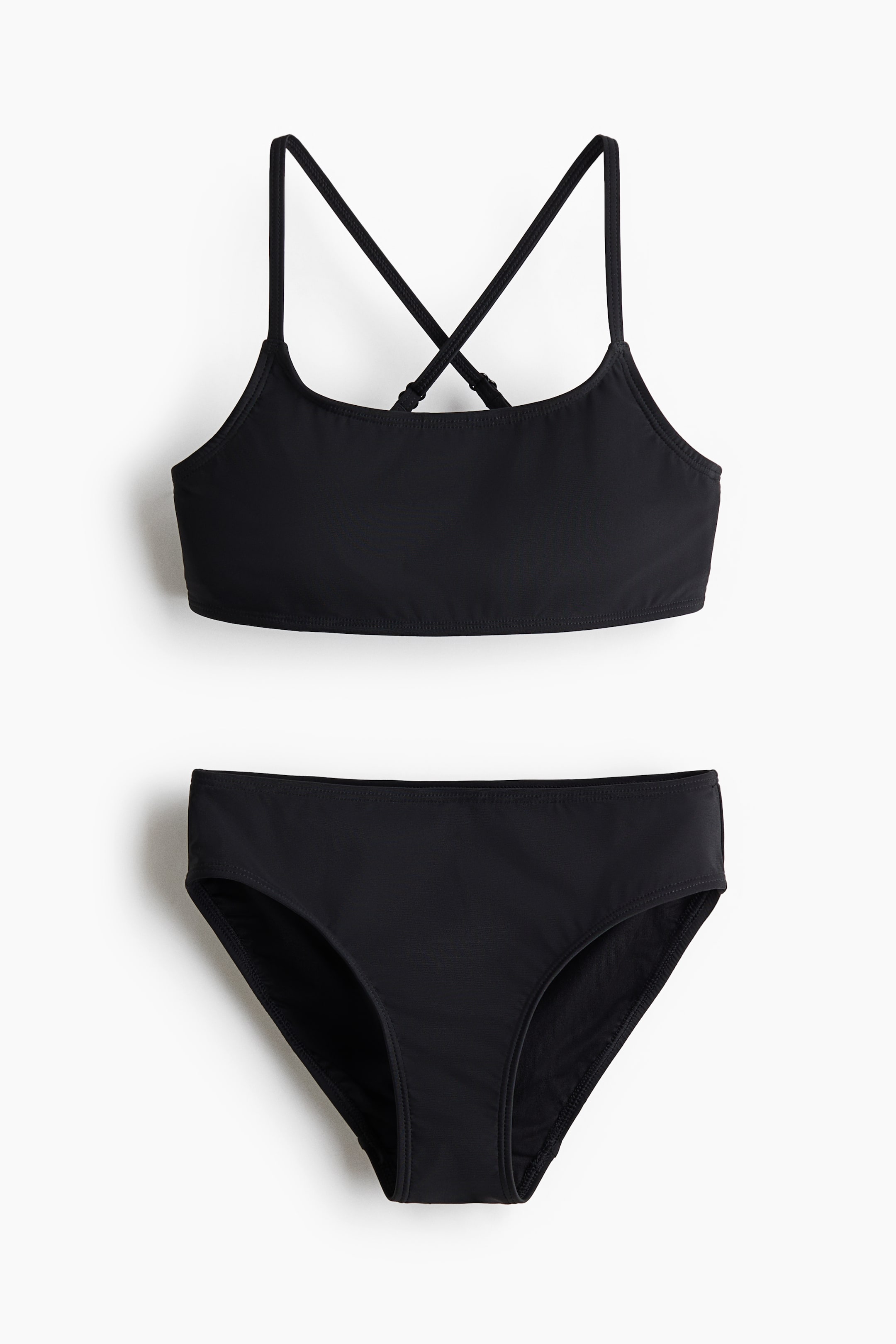 View larger image: A black two-piece swimsuit featuring a crop top with thin shoulder straps that crisscross at the back, and a matching classic hip-cut bikini brief.