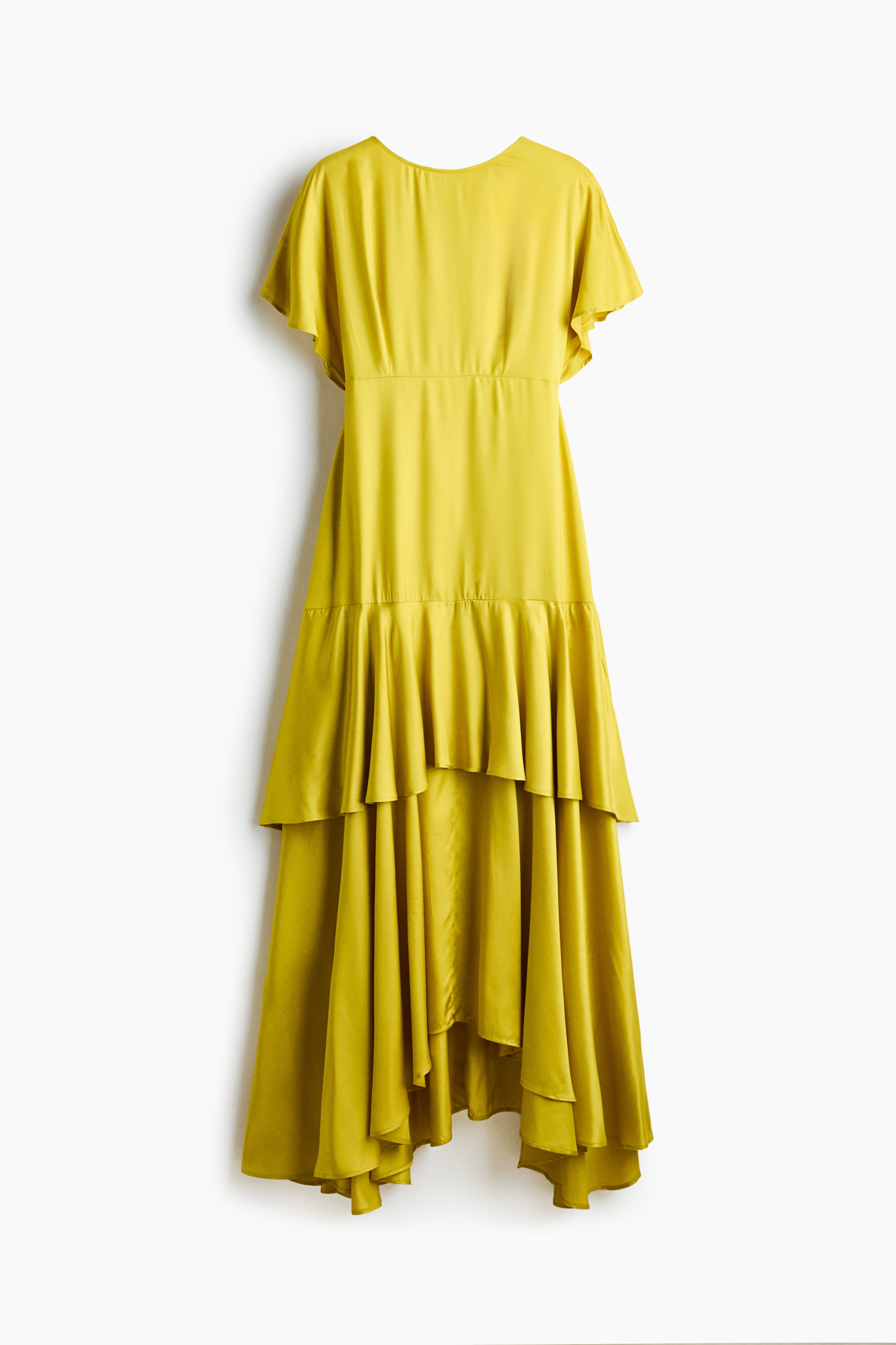 The model is wearing a long yellow dress featuring a round neckline, short butterfly sleeves, a fitted waist seam, and a tiered skirt with a flounce. She is posing with her hands placed behind her hips, highlighting the dressâs flowing high-low hem.