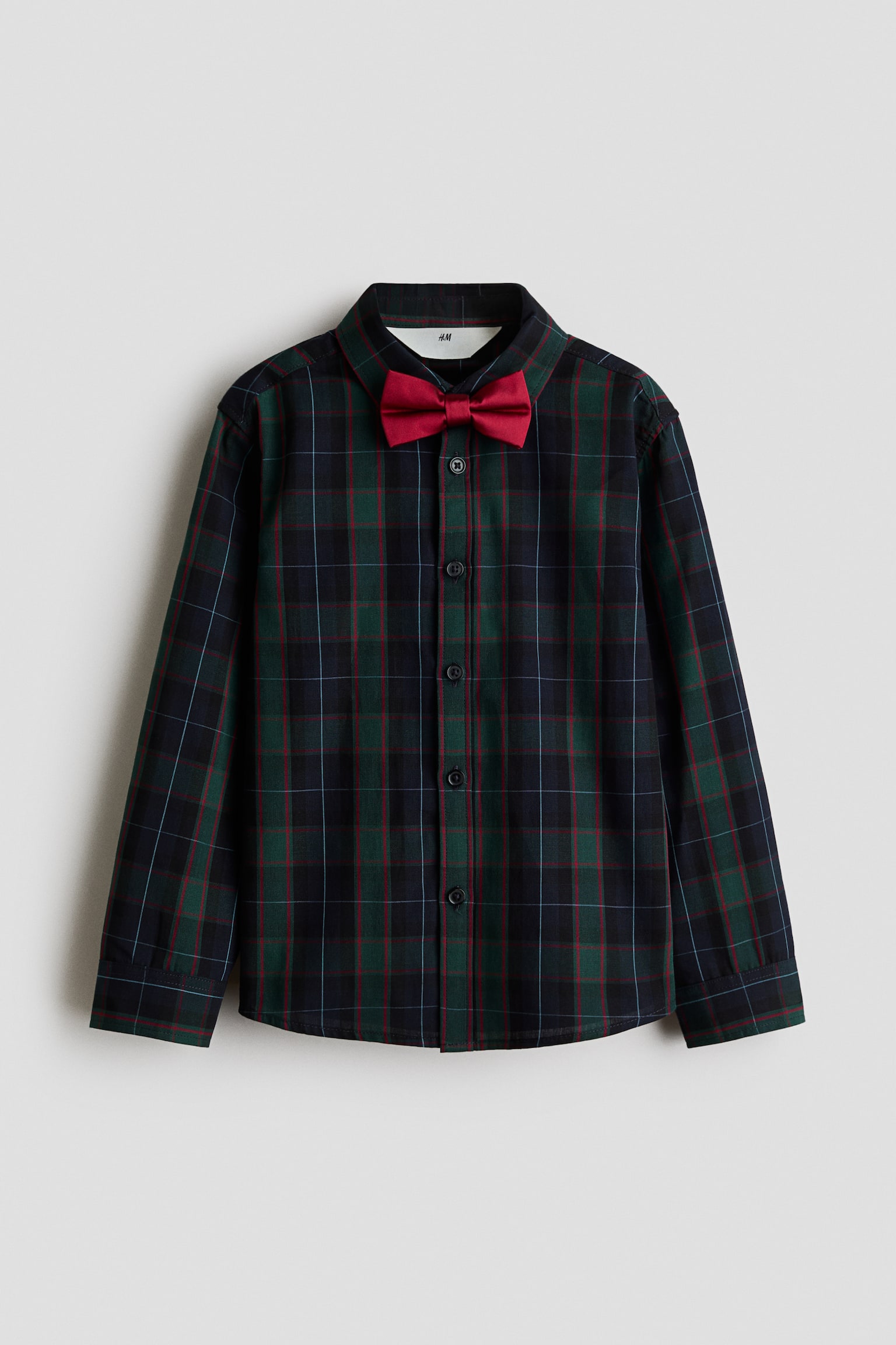 Une chemise en coton Ã  manches longues Ã  carreaux vert foncÃ© et bleu marine, vue de face, est rehaussÃ©e dâun nÅud papillon en satin rouge uni au col. La chemise prÃ©sente un col Ã  pointes rabattues, une patte de boutonnage avec des boutons foncÃ©s et des manches longues avec poignets boutonnÃ©s.